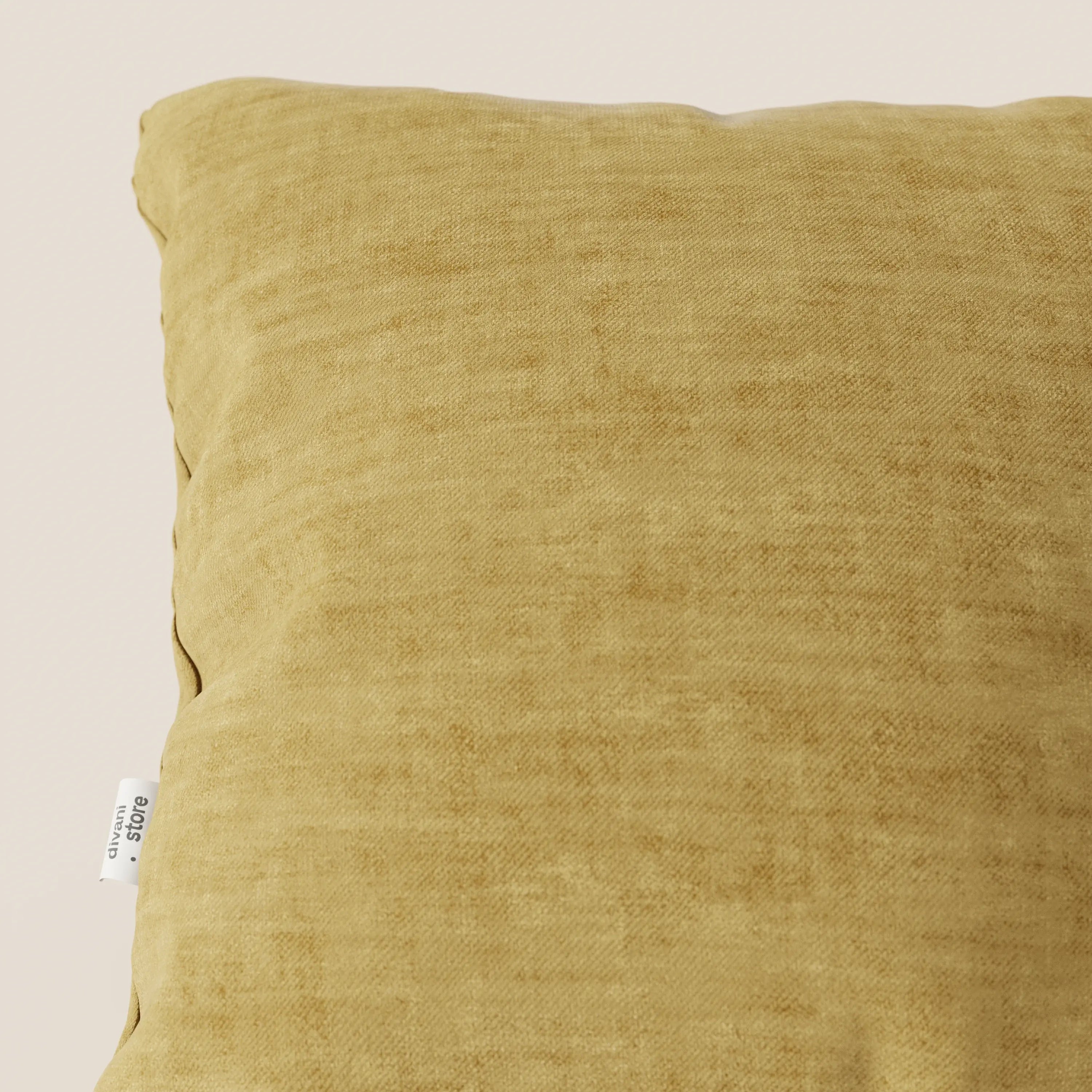 Primo piano del cuscino Sofia di Divani.Store in velluto nuvolato giallo-oro Easy Clean T35, parzialmente visibile su uno sfondo chiaro. Una piccola etichetta bianca con testo nero si trova sul bordo sinistro, evidenziando il suo tessuto morbido e antimacchia.