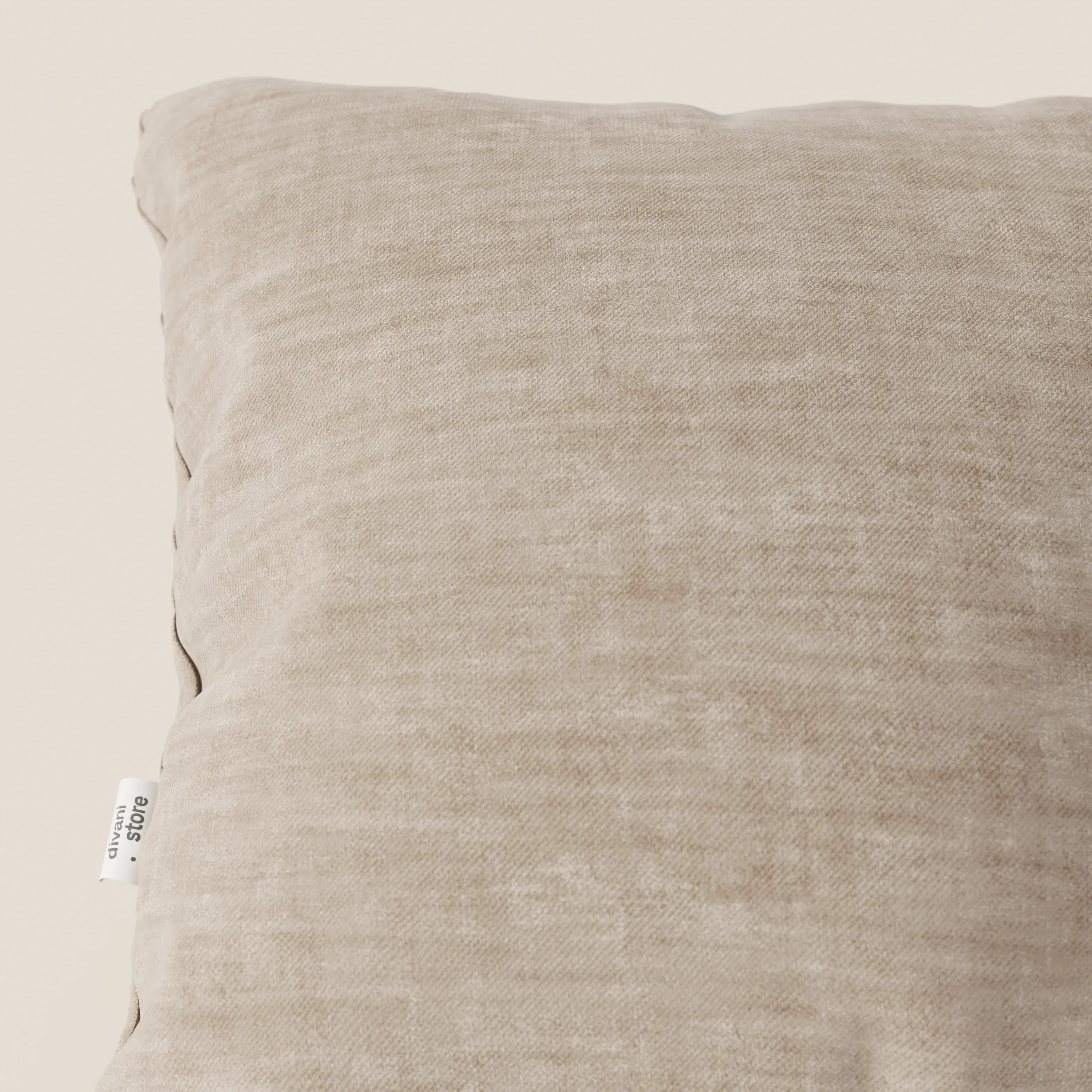 Primo piano del cuscino Sofia beige di Divani.Store, realizzato in morbido velluto nuvolato (Easy Clean T35), con una piccola etichetta bianca sulla cucitura. Lo sfondo è un semplice bianco sporco.
