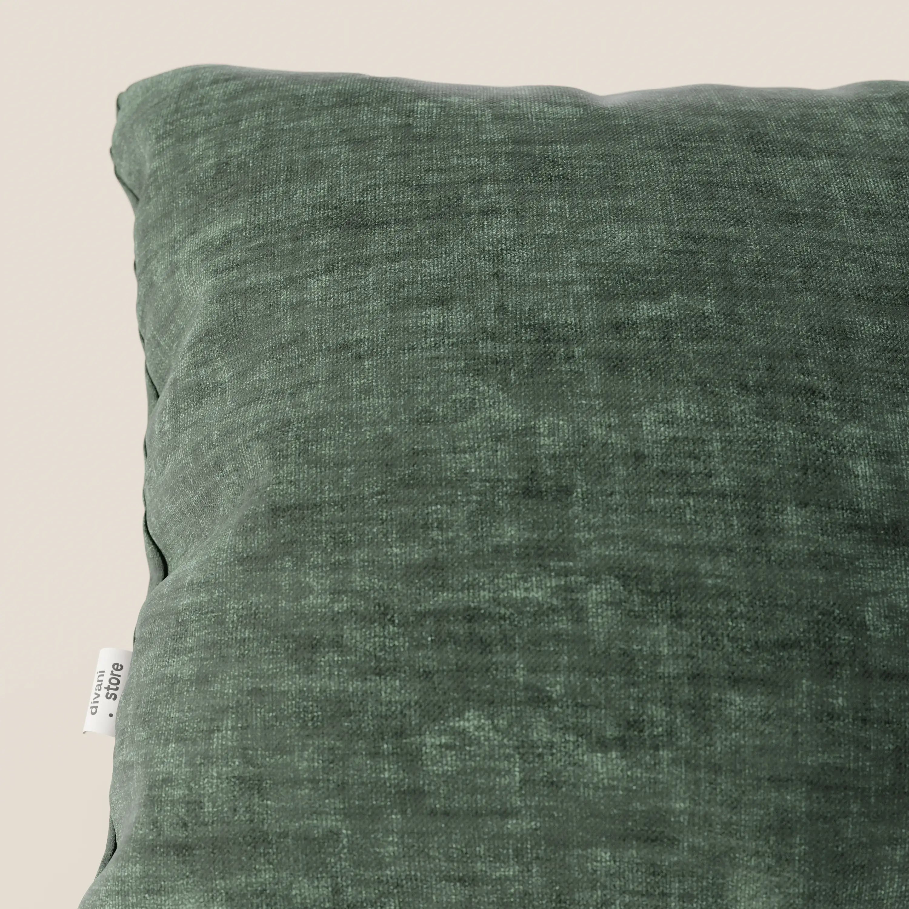 Primo piano del cuscino Sofia di Divani.Store in verde scuro, realizzato in morbido velluto nuvolato impermeabile e antimacchia (Easy Clean T35), con etichetta bianca sul lato. Lo sfondo bianco sporco mette in risalto la consistenza felpata e i dettagli sottili.