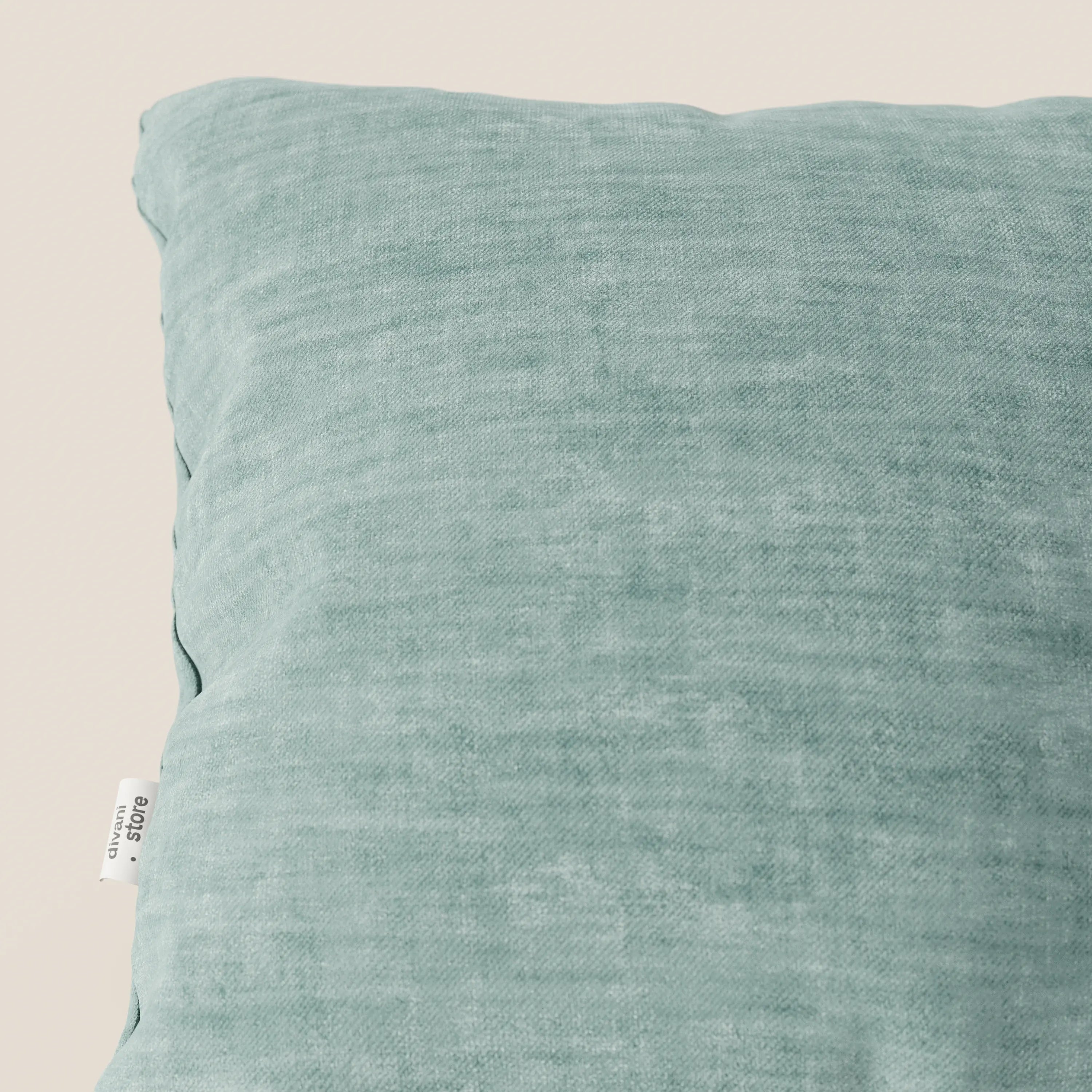 Primo piano del cuscino Sofia verde chiaro di Divani.Store, realizzato in morbido velluto Easy Clean T35 impermeabile e antimacchia. Il cuscino quadrato presenta un'etichetta di tessuto visibile sul lato sinistro e poggia su uno sfondo neutro.