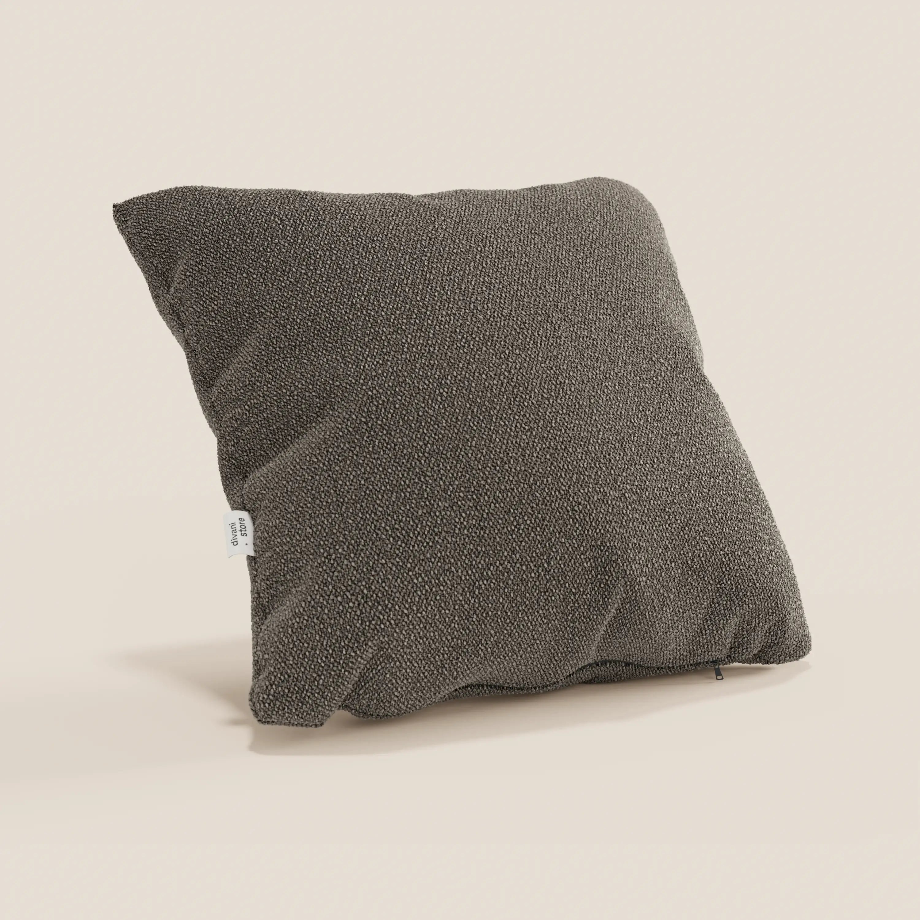 Un cuscino Lambada quadrato di colore marrone scuro di Divani.Store, realizzato in tessuto T33 lavabile e impermeabile simile al cotone fresco, si trova in posizione obliqua su uno sfondo beige chiaro. Una piccola etichetta bianca è attaccata sul lato, con una cerniera visibile sul bordo inferiore.