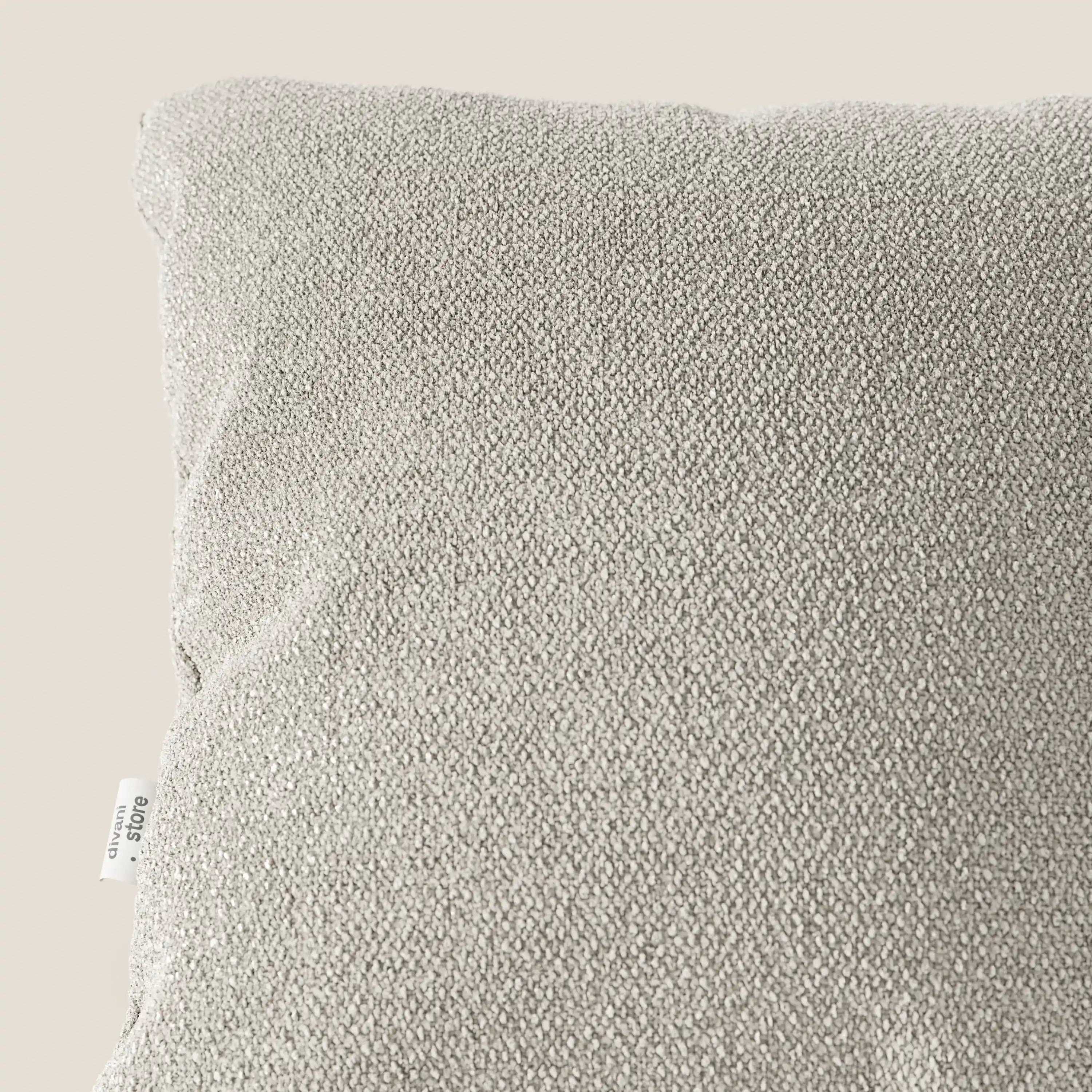 Primo piano di un cuscino Lambada grigio chiaro di Divani.Store, realizzato in tessuto naturale simil-cotone fresco, antimacchia e impermeabile. Nell'angolo in alto a sinistra si nota un'etichetta bianca con testo nero sulla cucitura laterale su uno sfondo a tinta unita.