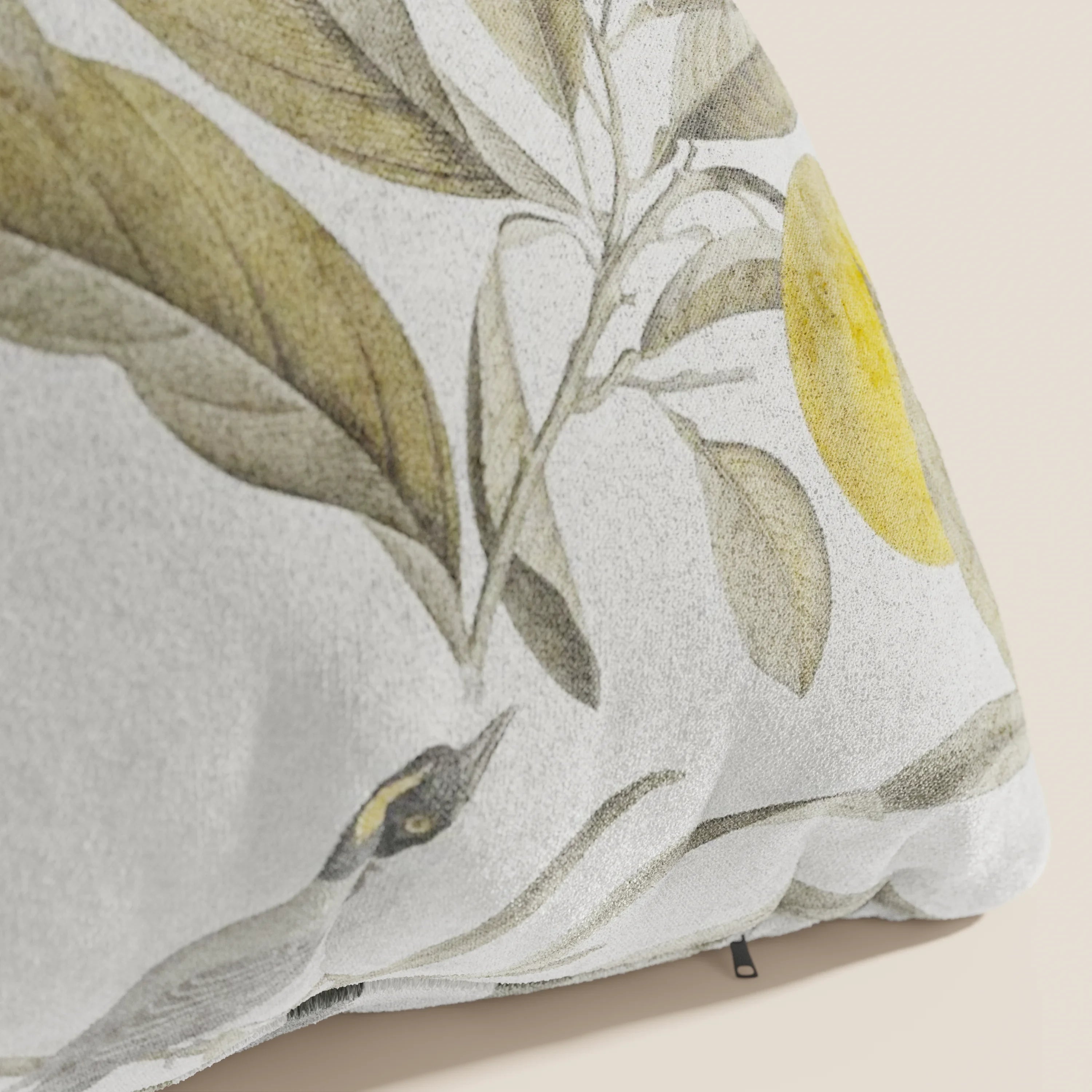 Primo piano della collezione Lemon elegante di cuscini a fantasia in velluto impermeabile panna di Divani.Store, che mostra foglie verdi, frutti gialli e un uccello su sfondo bianco con tessuto morbido e una cerniera sulla cucitura.