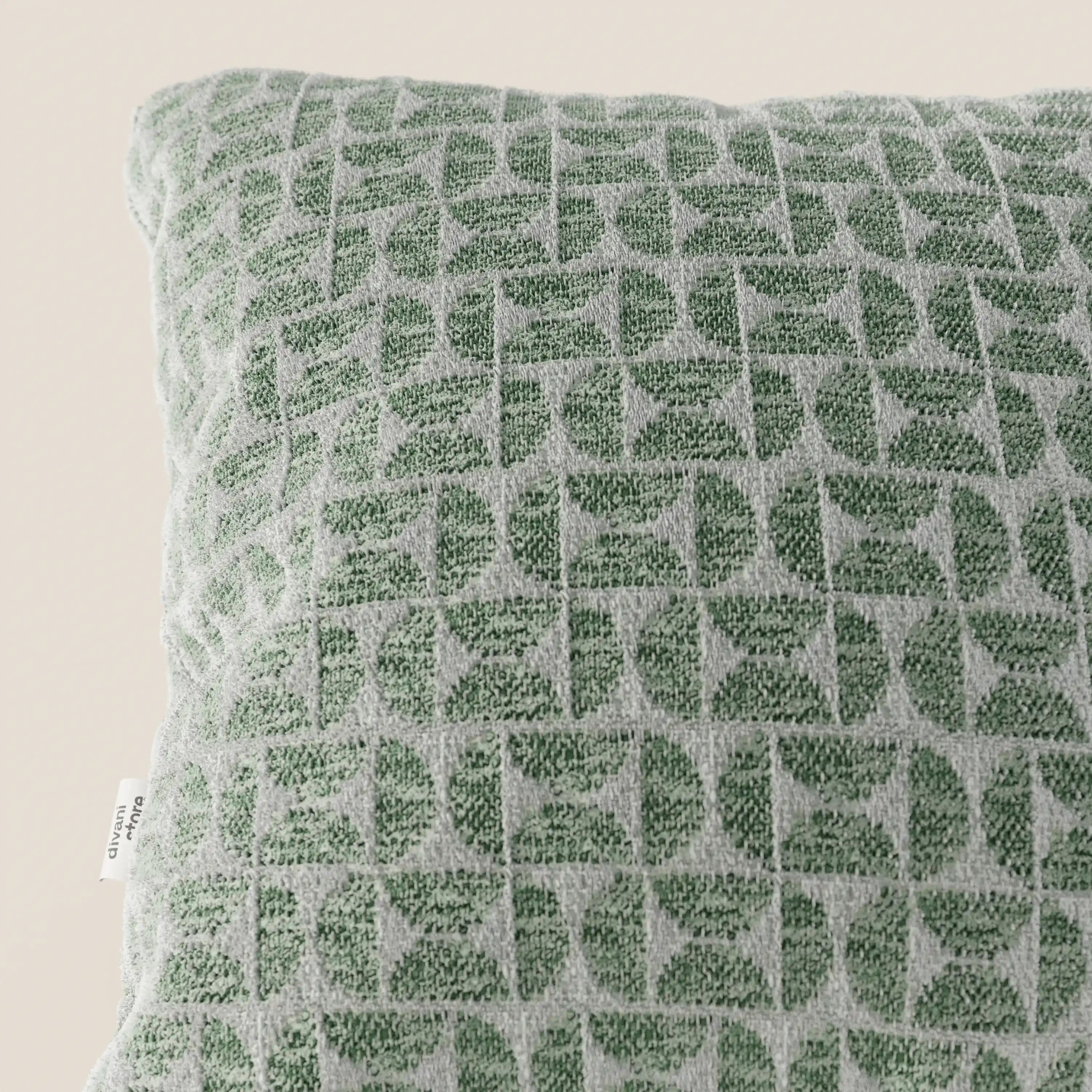 Un primo piano del cuscino Naxos Decoro 45x45 in lino di Divani.Store mette in risalto un elegante motivo geometrico a foglie nei toni del verde e del grigio chiaro, con una piccola etichetta in tessuto bianca sul lato, il tutto su uno sfondo beige.