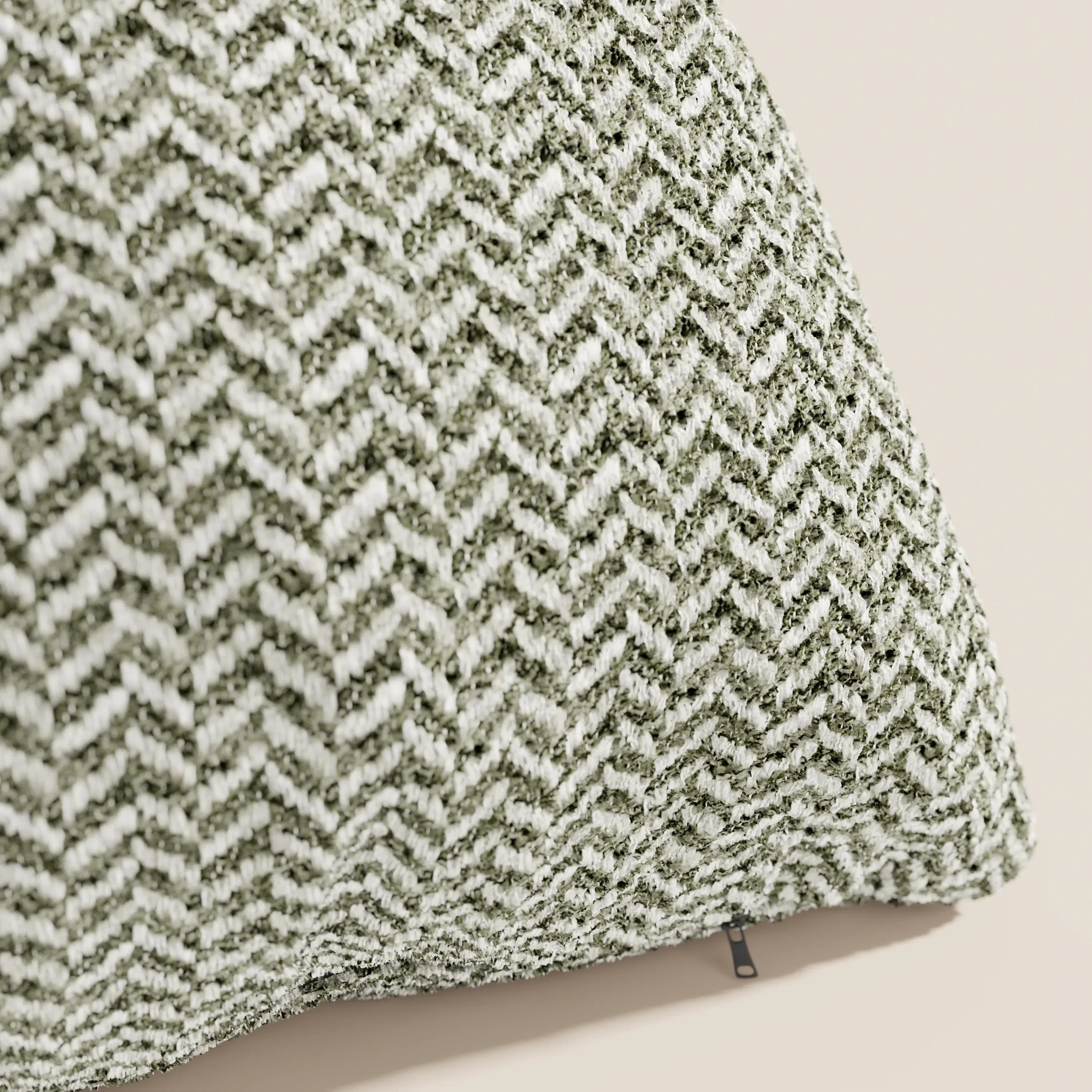 Un primo piano del cuscino Sorrento 45x45 in lino di Divani.Store ne mette in risalto la trama a spina di pesce verde e bianca, lo sfondo beige chiaro e la piccola cerniera scura: l'ideale per chi cerca cuscini lavabili in lavatrice.