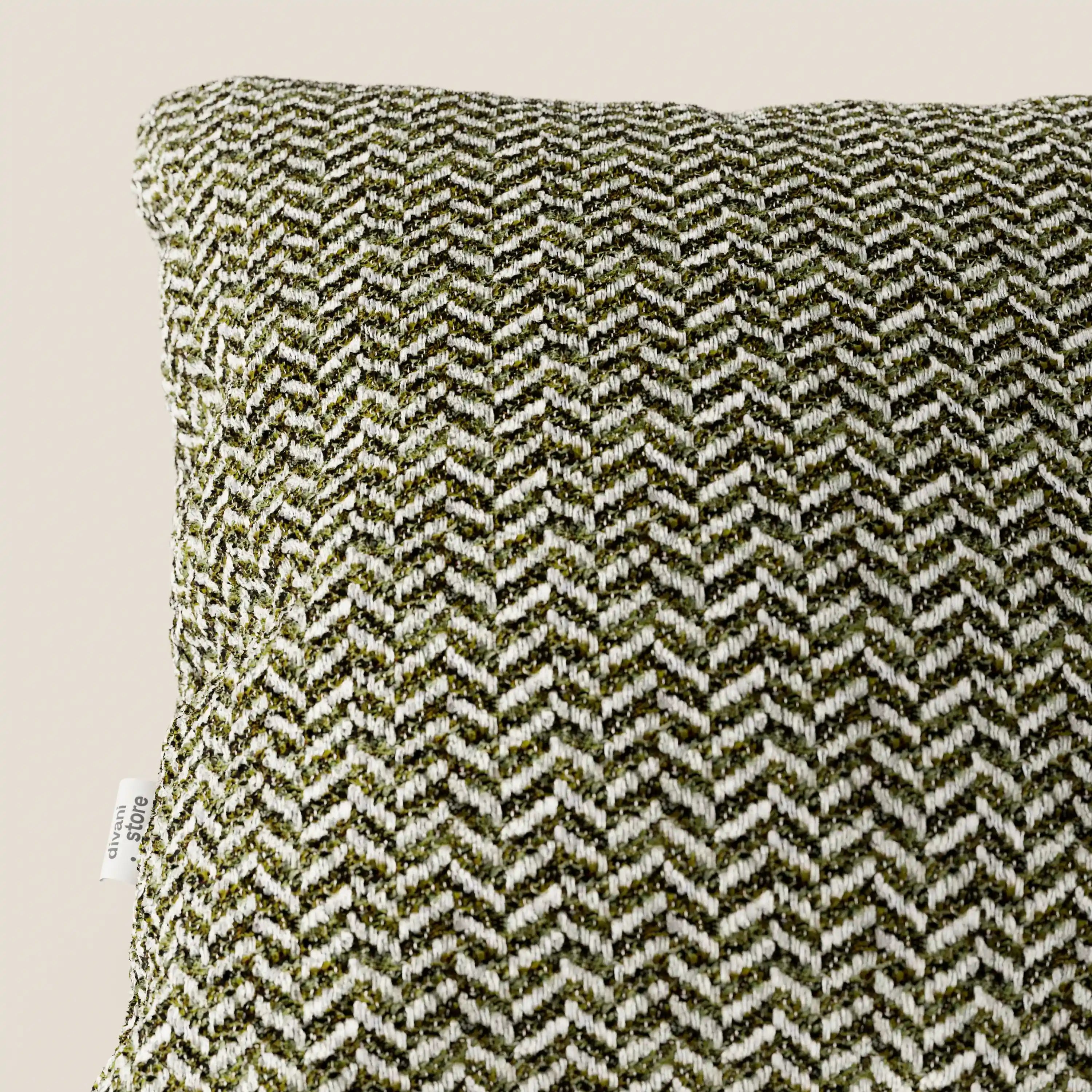 Un primo piano del cuscino Sorrento 45x45 in Lino di Divani.Store, caratterizzato da un motivo a spina di pesce verde e bianco, un morbido tessuto lavabile e una piccola etichetta bianca sul lato. Il tutto su uno sfondo beige chiaro a tinta unita.