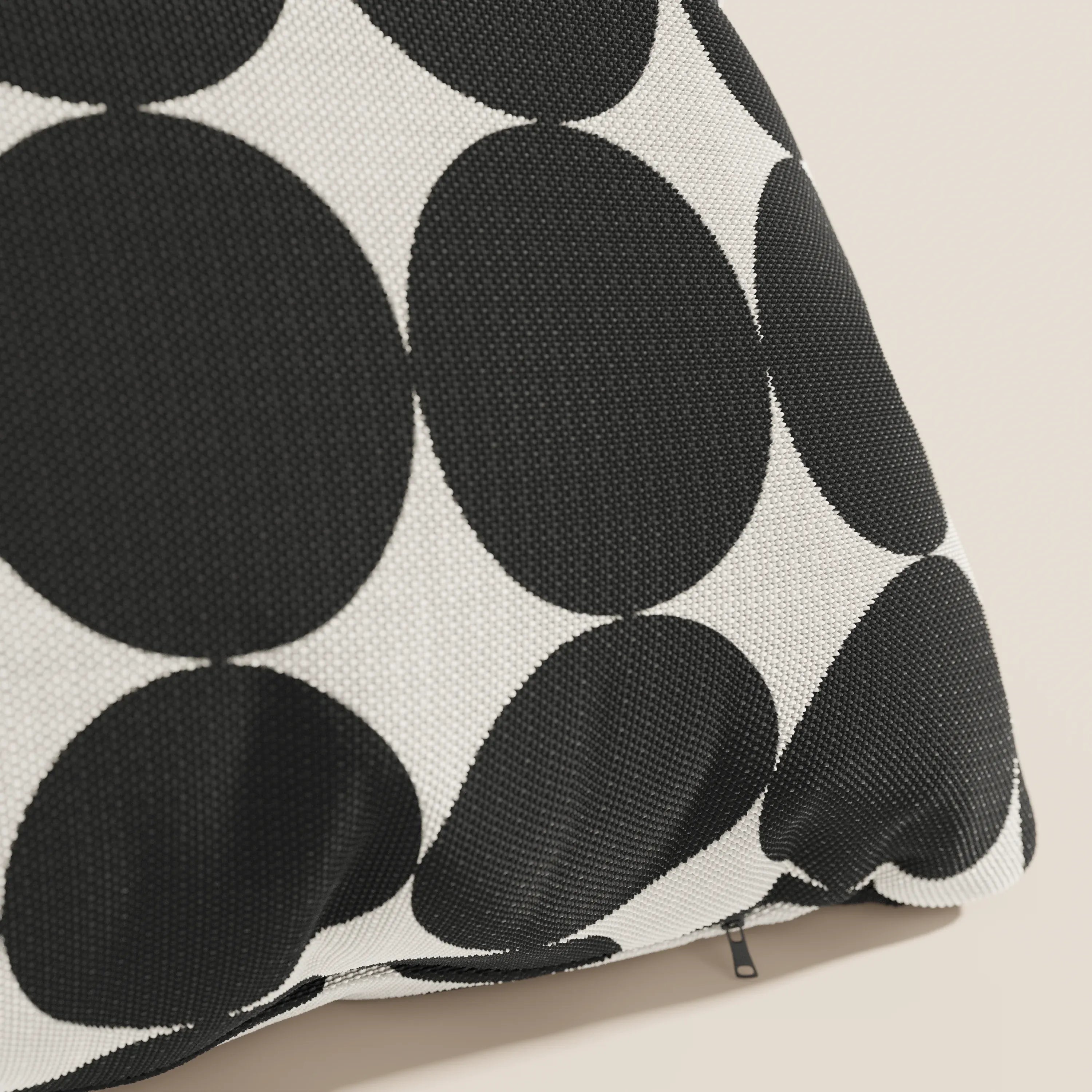 Un primo piano del cuscino geometrico Divani.Store Dot in idrorepellente nero, caratterizzato da un audace motivo a grandi cerchi in bianco e nero e da una cerniera leggermente visibile, su uno sfondo beige chiaro.