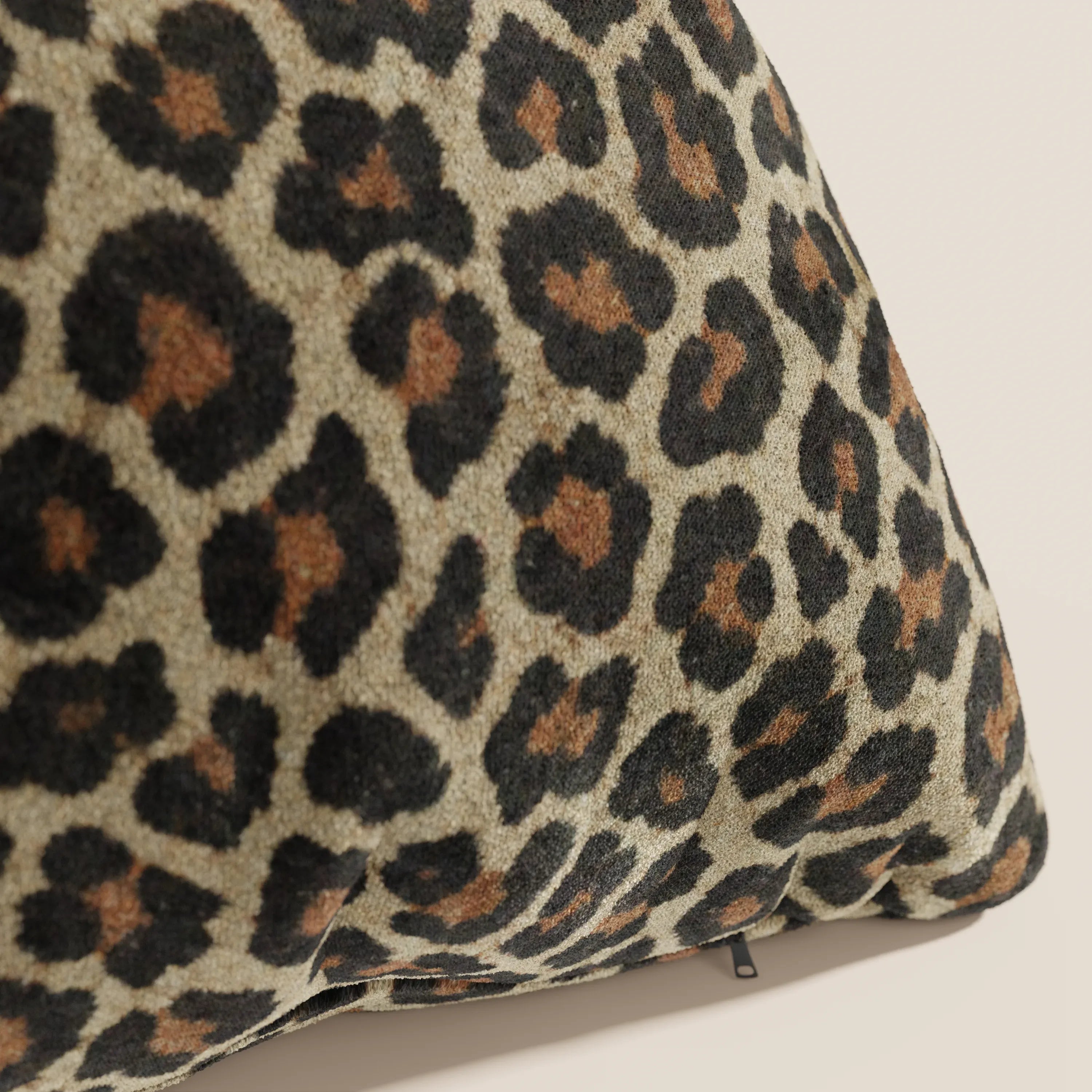Primo piano del cuscino Wild della collezione Wild di Divani.Store: un cuscino in microfibra impermeabile con stampa leopardata a macchie nere e marrone scuro su tinta unita, caratterizzato da una piccola cerniera nera sul bordo inferiore.