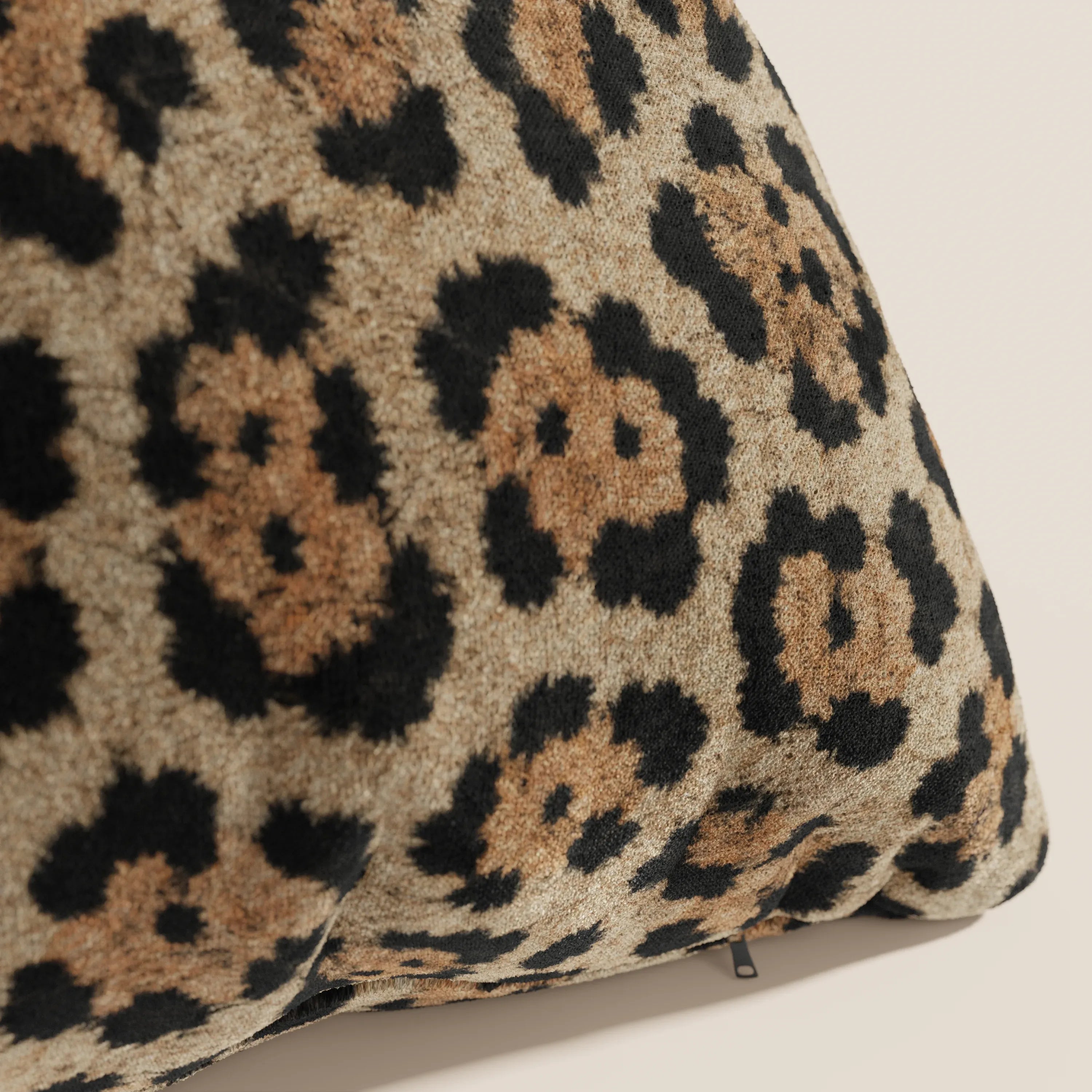 Primo piano del cuscino Divani.Store Wild della collezione Wild in microfibra impermeabile giaguaro, caratterizzato da un tessuto felpato e strutturato a motivi leopardati e da una cerniera a vista sul bordo inferiore su uno sfondo neutro.