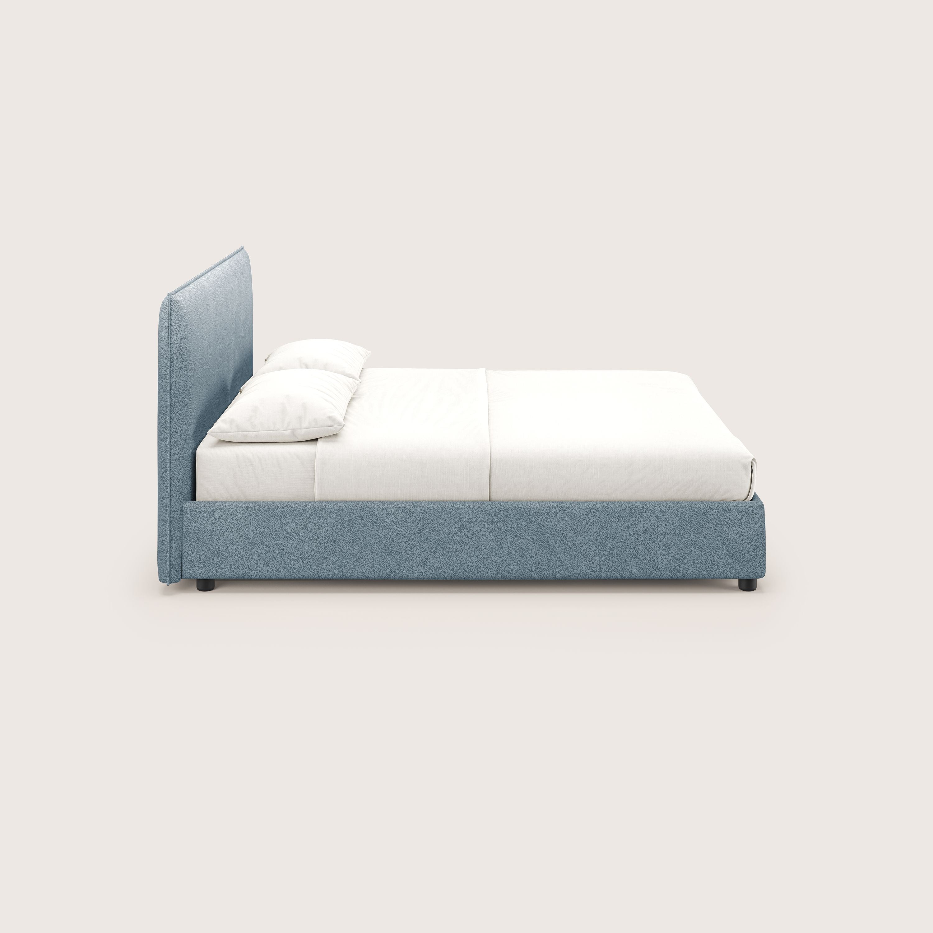 Il letto contenitore Nina di Letti.store è caratterizzato da un design italiano minimale in microfibra carta da zucchero lavabile, con struttura e testata imbottite, mostrato di lato con biancheria da letto bianca e due cuscini su uno sfondo bianco sporco.