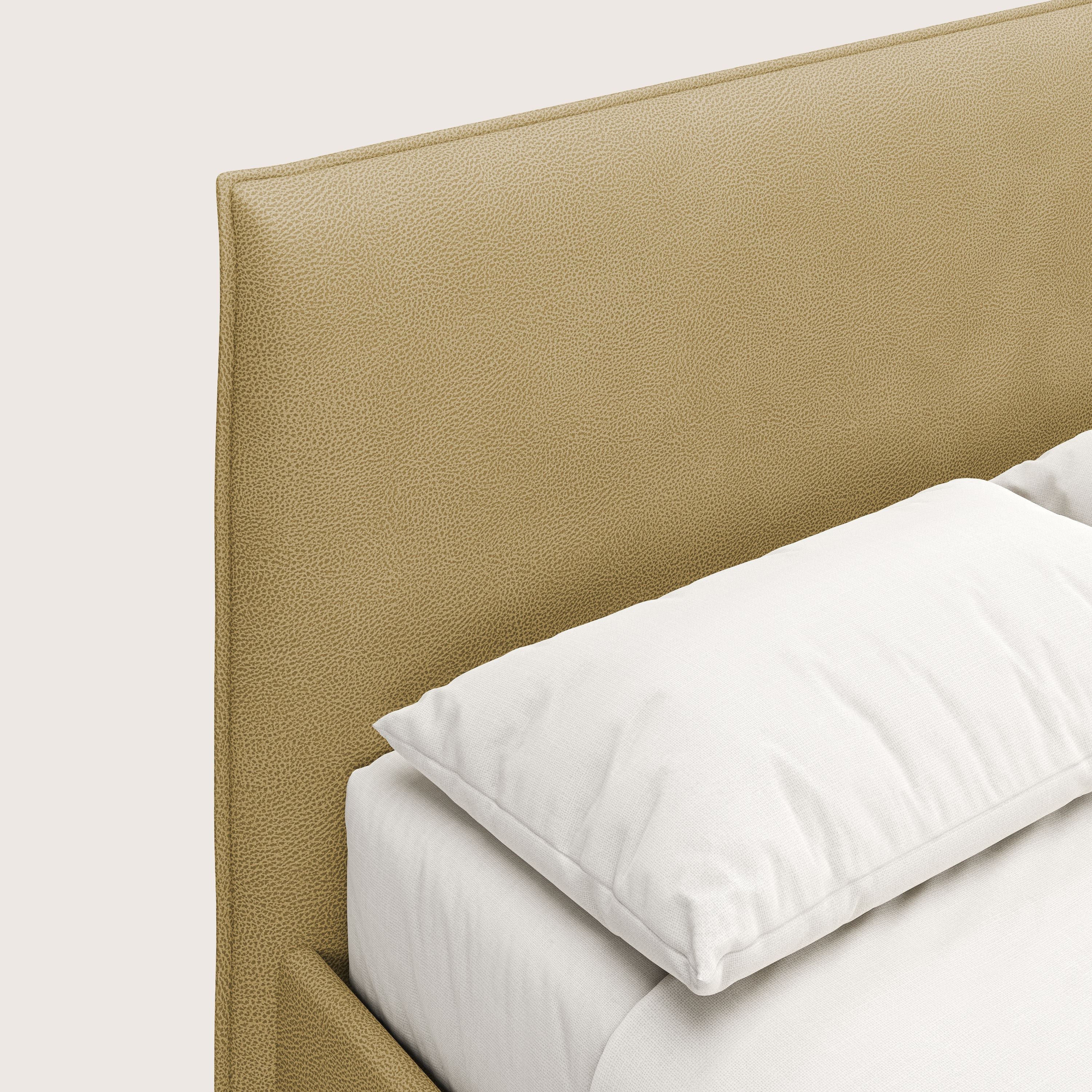 Primo piano del letto contenitore Nina di Letti.store dal design minimale, con testiera gialla in microfibra antimacchia effetto pelle e cuscino bianco su lenzuola bianche su sfondo chiaro.