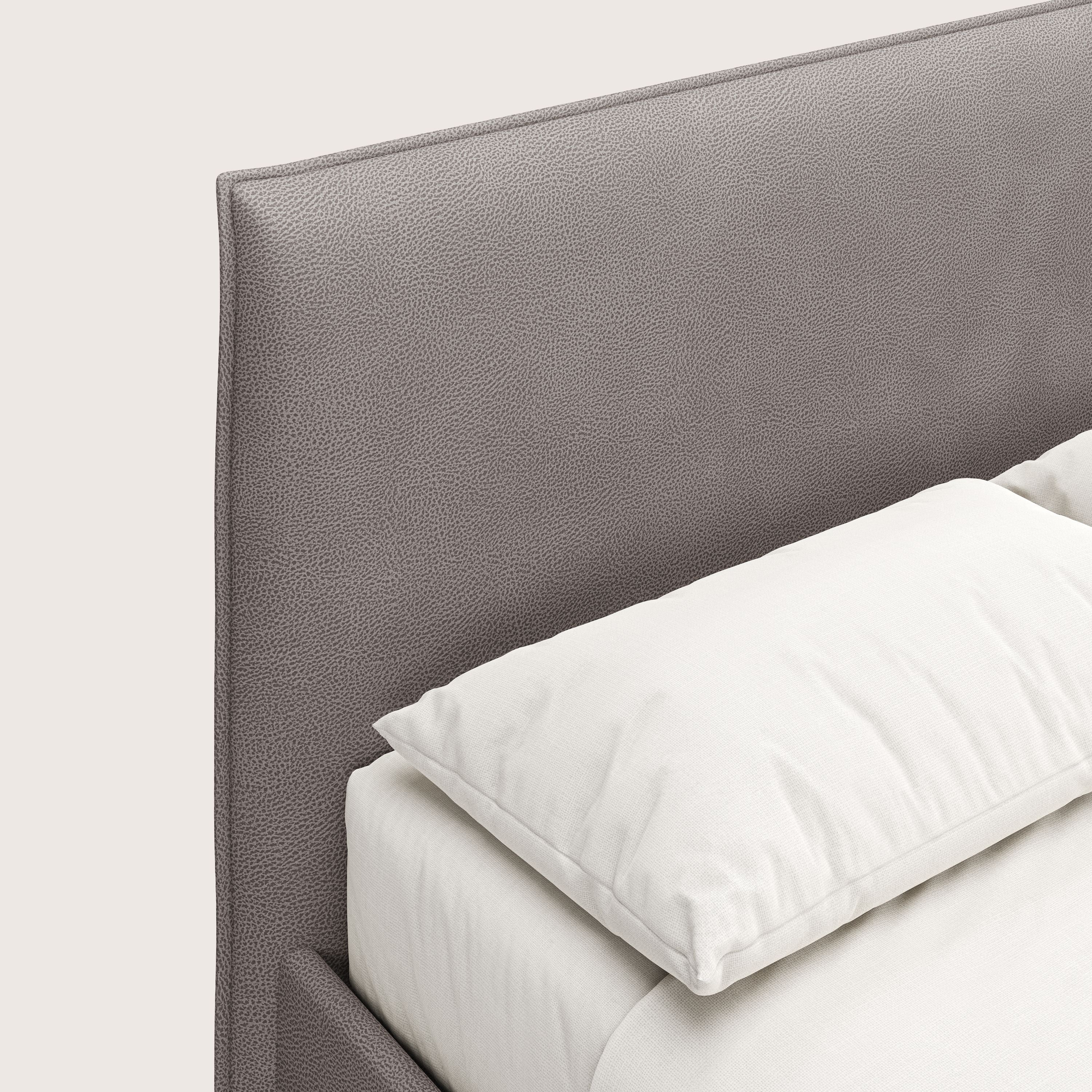 Un primo piano del letto contenitore Nina di Letti.store, caratterizzato da un design minimale in microfibra antimacchia color tortora con testiera imbottita, lenzuola e cuscino bianchi, il tutto su uno sfondo bianco sporco per un look italiano moderno.