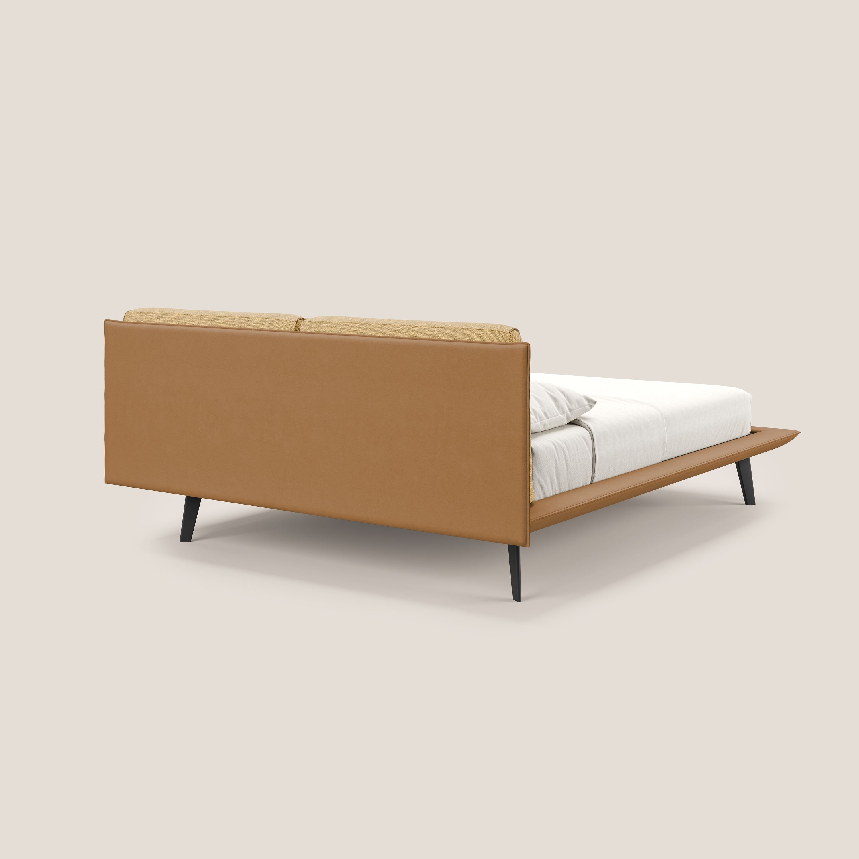 Il letto di design Petra di Letti.store è caratterizzato dal tessuto bicolore impermeabile T11/T06 cuoio-giallo, dai cuscini in piuma della testata e dalle gambe angolate in mogano. Nella foto dal lato posteriore, è vestita con biancheria da letto bianca su uno sfondo beige chiaro.