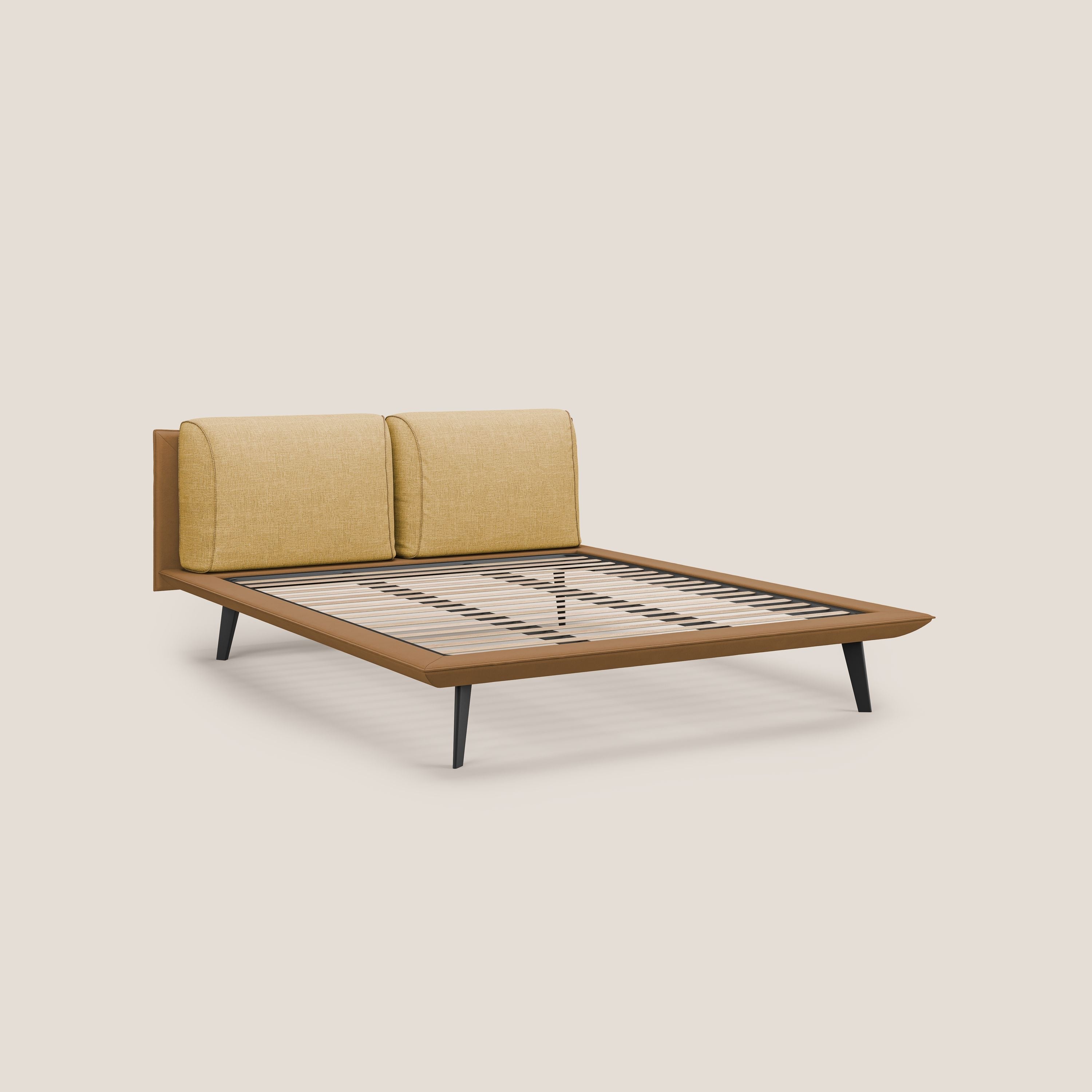 Il letto di design Petra di Letti.store è caratterizzato da tessuto impermeabile bicolore (T11 e T06 cuoio - giallo), cuscini in piuma, testata imbottita giallo senape e gambe angolate in mogano. Il materasso non mostra la rete ortopedica a doghe. Sfondo beige a tinta unita.