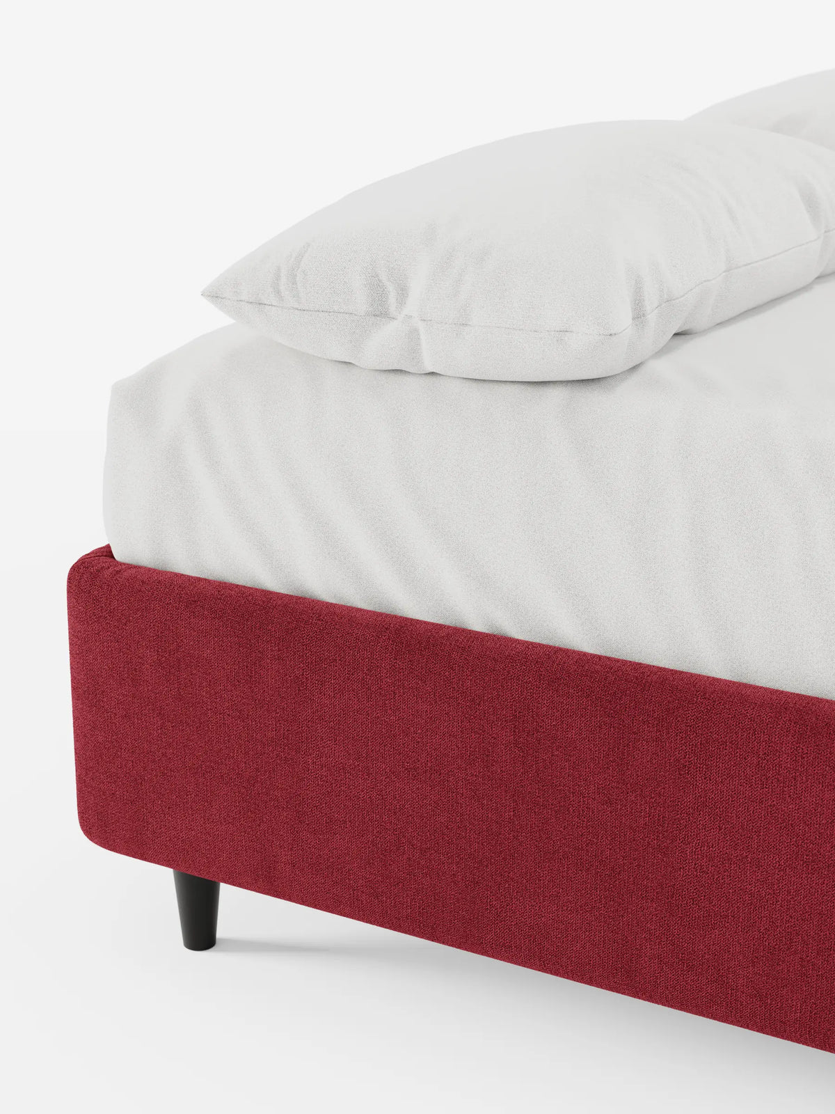 Un primo piano di un letto sommier imbottito ERON con vano contenitore in tessuto impermeabile certificato Oeko-Tex, con struttura rossa e gambe cilindriche scure, su cui spicca la biancheria da letto bianca su uno sfondo a tinta unita.