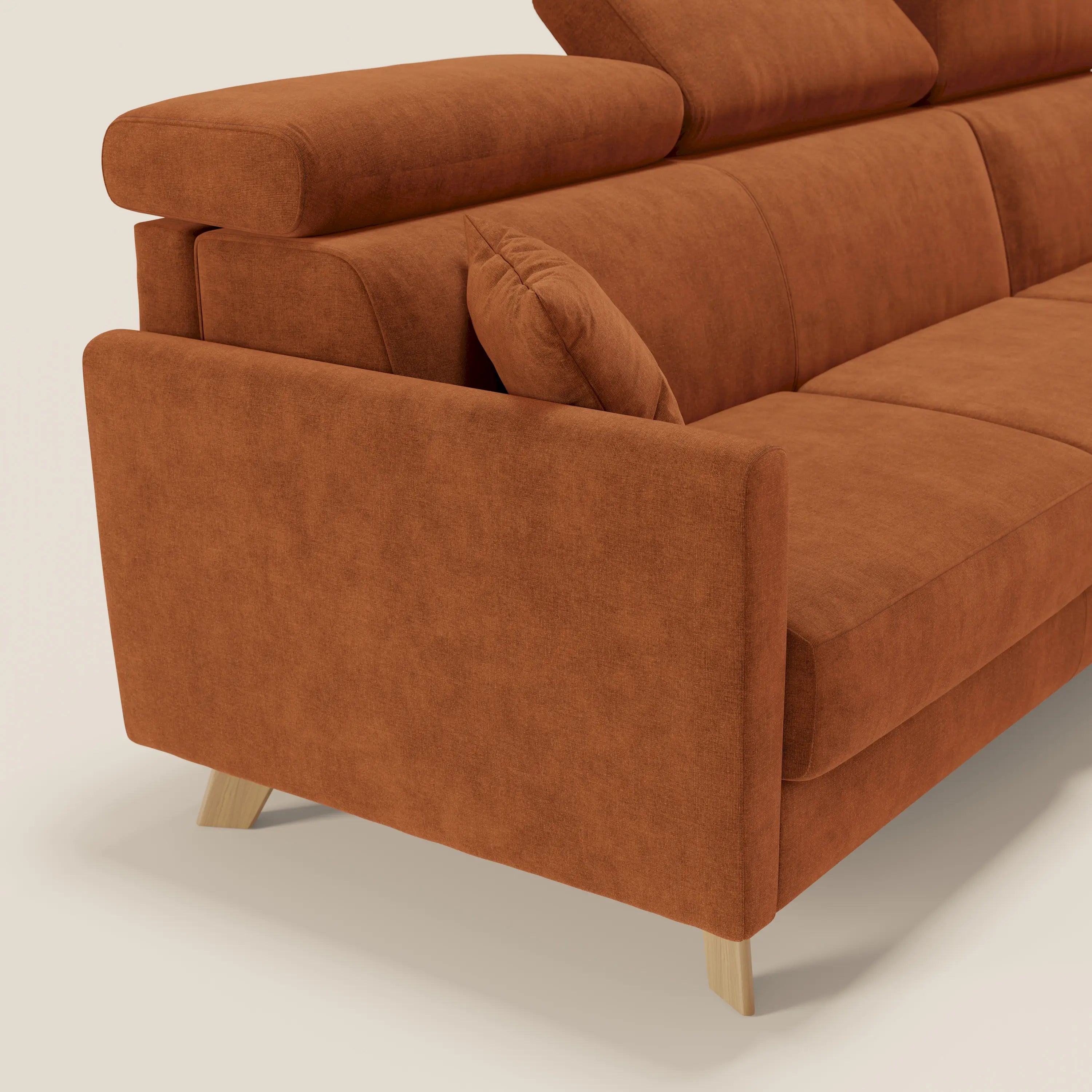 Primo piano del divano letto angolare sfoderabile Francy di Divani.Store in tessuto antimacchia T17 arancione, con poggiatesta reclinabili, cuscino angolare Comfort Smart, braccioli sottili, poltrona contenitore e gambe in legno chiaro su uno sfondo neutro.