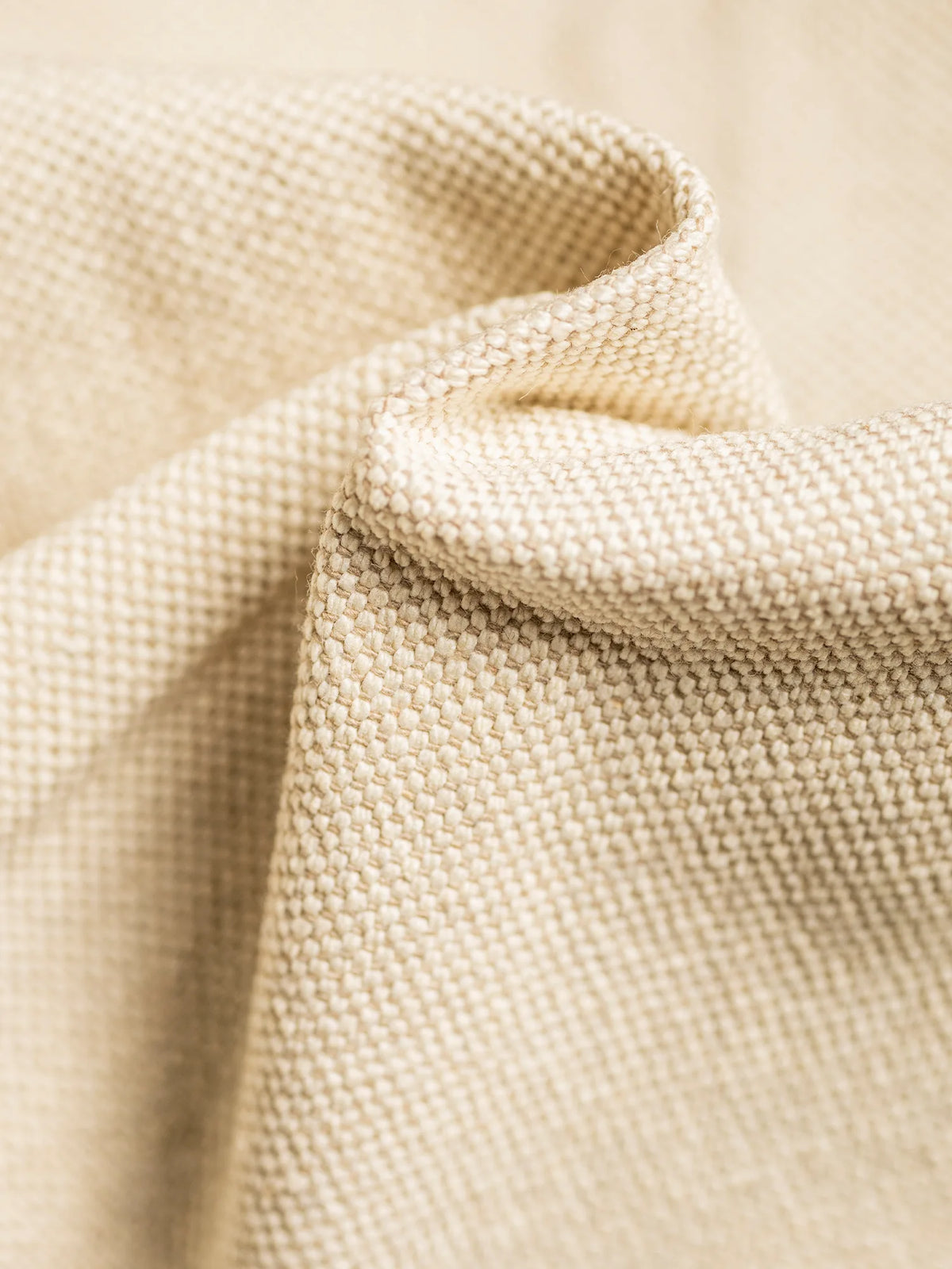 Primo piano del tessuto S06 LINOSA, 100% cotone riciclato, Made in Italy, color beige, caratterizzato da una trama intrecciata effetto canapa che cade in morbide pieghe per mettere in risalto il suo motivo resistente a griglia.
