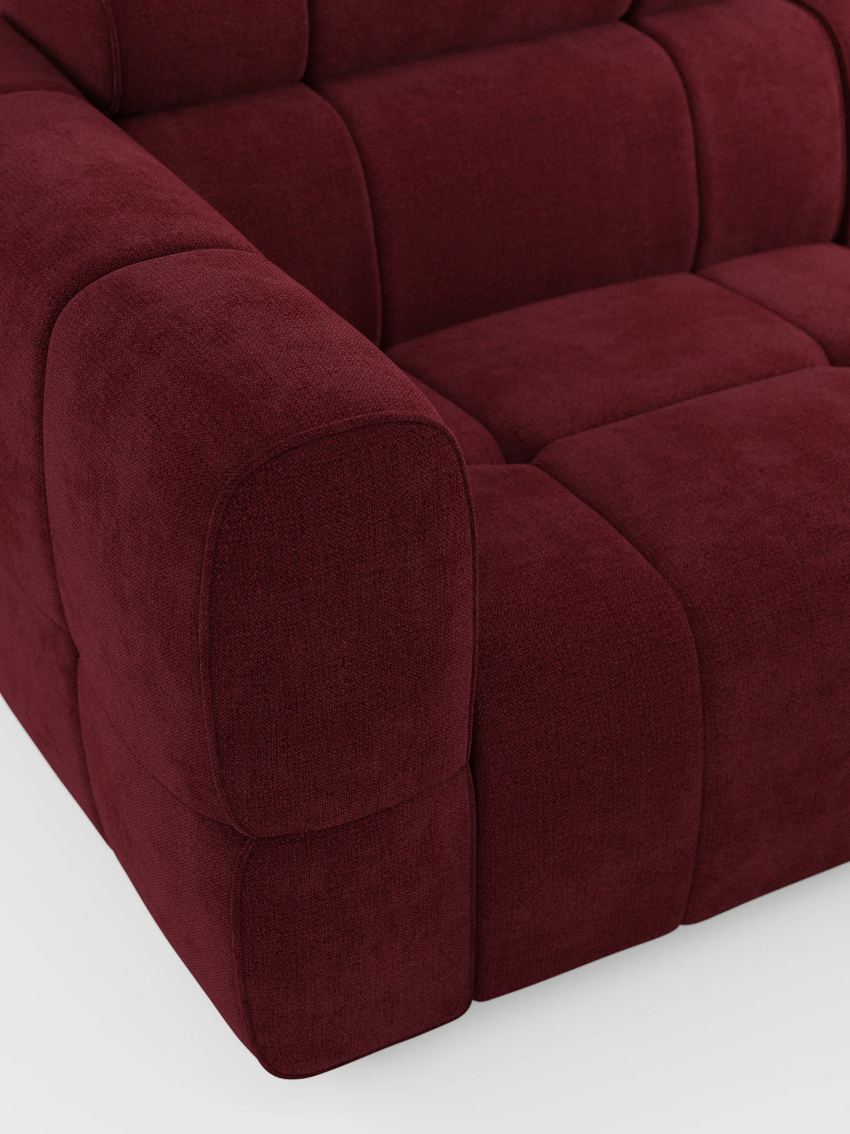 Un primo piano del divano angolare modulare Giotto a 5 posti da 296 cm con penisola e funzione relax elettrica opzionale, rivestito in tessuto smacchiabile T23 color bordeaux scuro, caratterizzato da tessuto testurizzato, cuscini con cuciture a quadrati e un ampio bracciolo arrotondato di colore bianco.