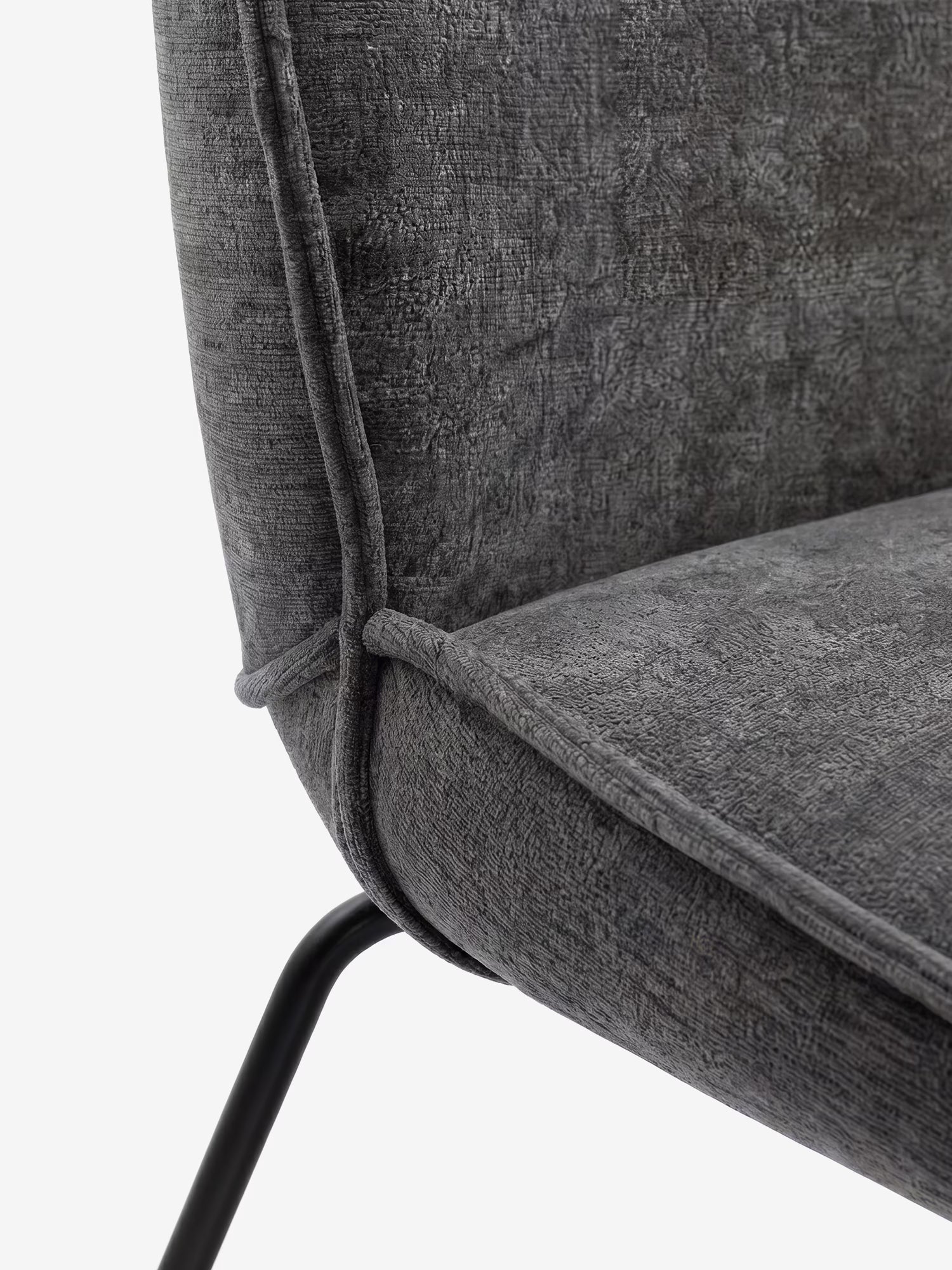 Primo piano della sedia "Iride", imbottita in morbido tessuto materico di Divani.Store, caratterizzata da un tessuto grigio scuro dalla trama ruvida, uno schienale curvo con cuciture a vista e bordino, e gambe in metallo nero su uno sfondo bianco a tinta unita.