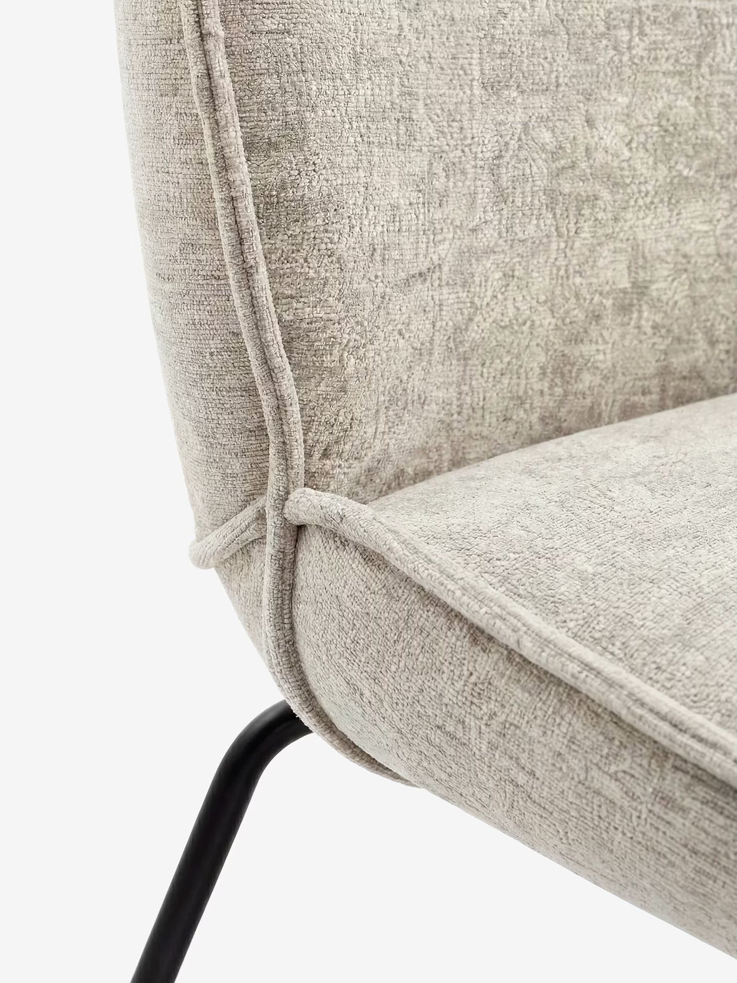 Primo piano della sedia imbottita Iride di Divani.Store, caratterizzata da un rivestimento beige chiaro dalla texture morbida al tatto con cuciture a vista, seduta e schienale curvi e un'elegante base in metallo nero che le conferisce un look minimalista e contemporaneo.