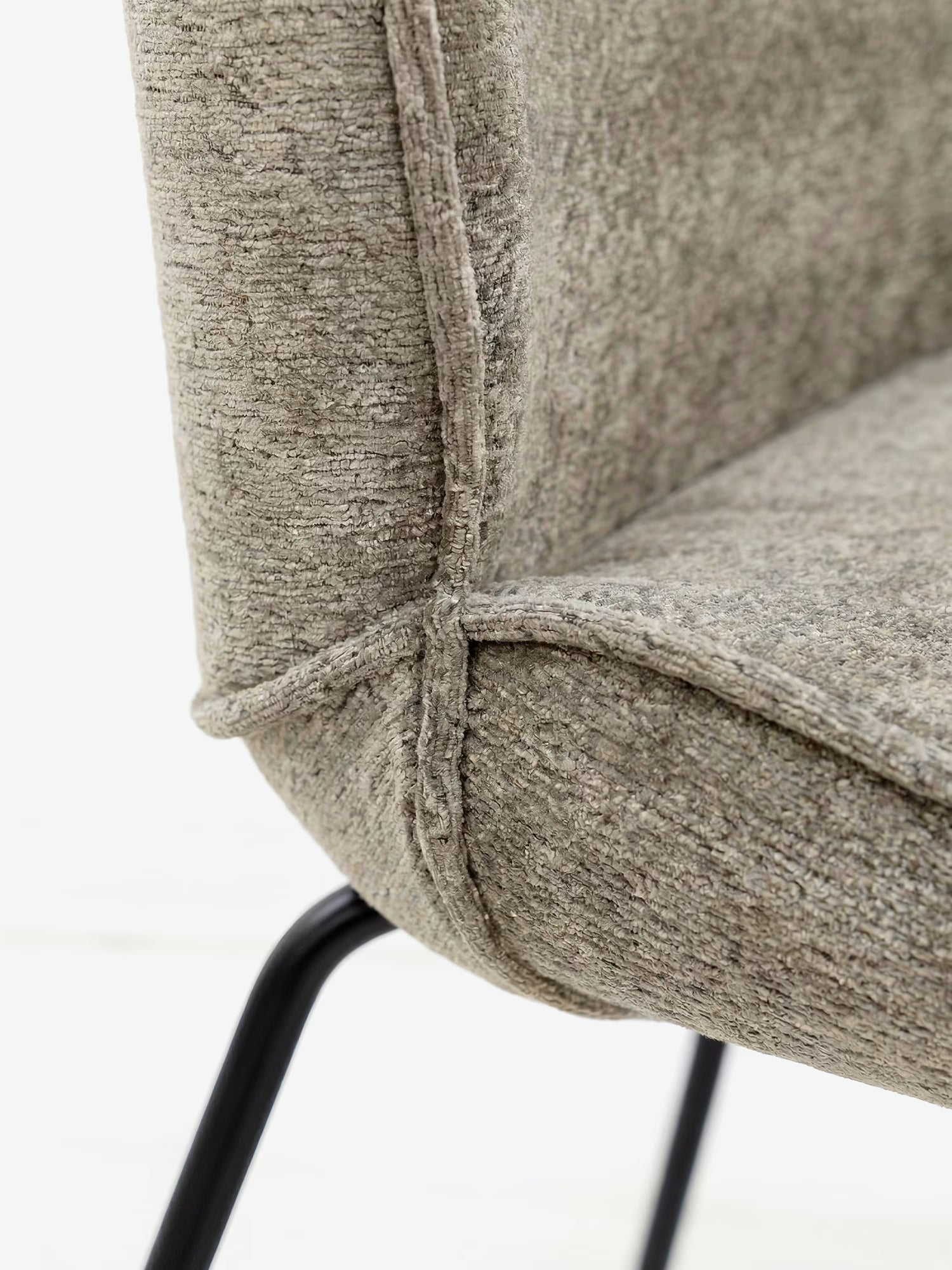 Primo piano della sedia imbottita “Iride” in morbido tessuto materico di Divani.Store, caratterizzata da un tessuto marrone-grigiastro con texture e cuciture a vista, e da una struttura in metallo nero su sfondo bianco.