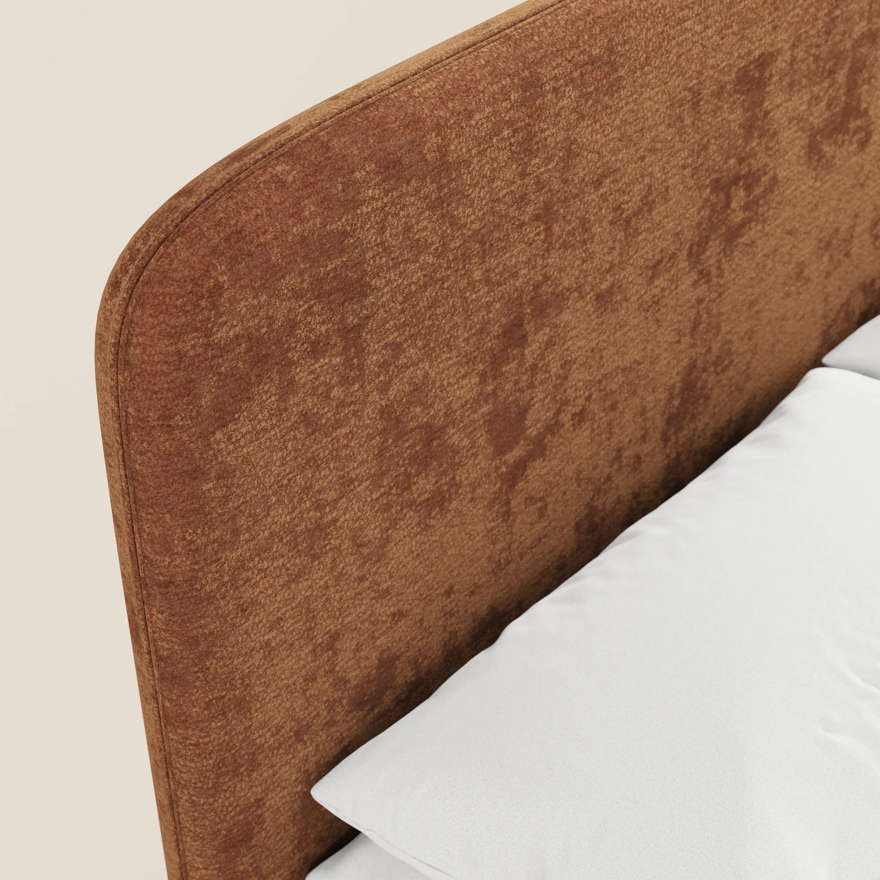 Primo piano del letto imbottito KAELOS Letto Minimal di Letti.store, caratterizzato da una testiera in morbido tessuto ciniglia con bordi arrotondati, gambe alte e vano contenitore. In basso a destra, su uno sfondo beige chiaro, spicca la biancheria da letto di un bianco brillante.