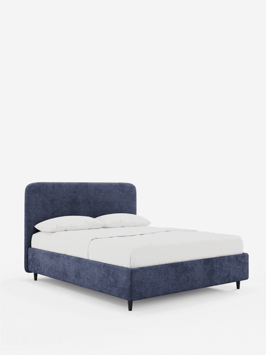Un letto KAELOS, modello minimal imbottito in tessuto ciniglia testurizzato blu intenso, spicca su uno sfondo bianco, caratterizzato da una testiera arrotondata, linee pulite e gambe scure e slanciate.