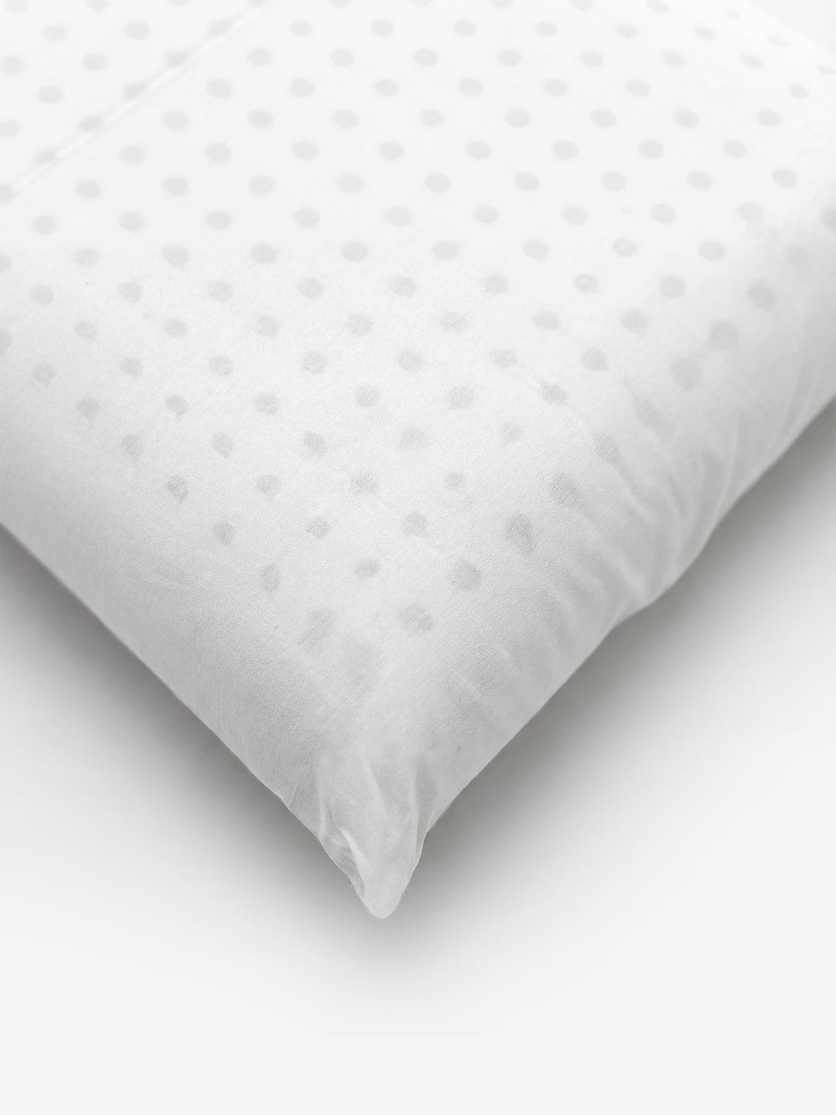 Viene mostrato un primo piano del VELTHA-FLOW – Guanciale bio-adattivo in Lattice Alveolato 100% Naturale di Divani.Store: si tratta di un cuscino bianco con un delicato motivo a pois grigio chiaro sulla superficie liscia del tessuto, riposto su uno sfondo bianco. Nell’immagine è visibile solo un angolo del cuscino.