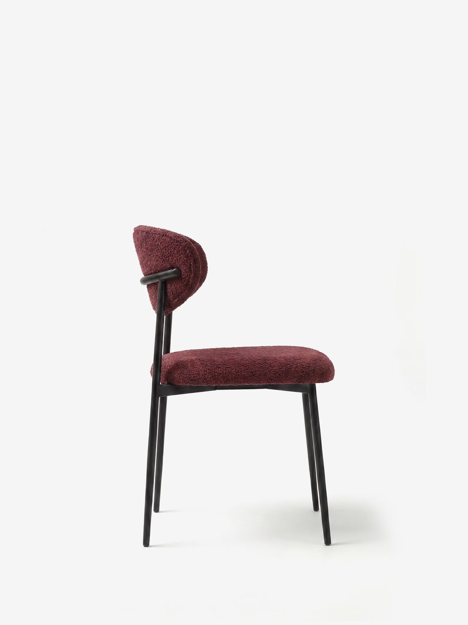 La poltrona imbottita in morbido tessuto ciniglia di Divani.Store, con seduta e schienale curvi color bordeaux e struttura minimalista in metallo nero, è raffigurata di profilo su uno sfondo bianco.