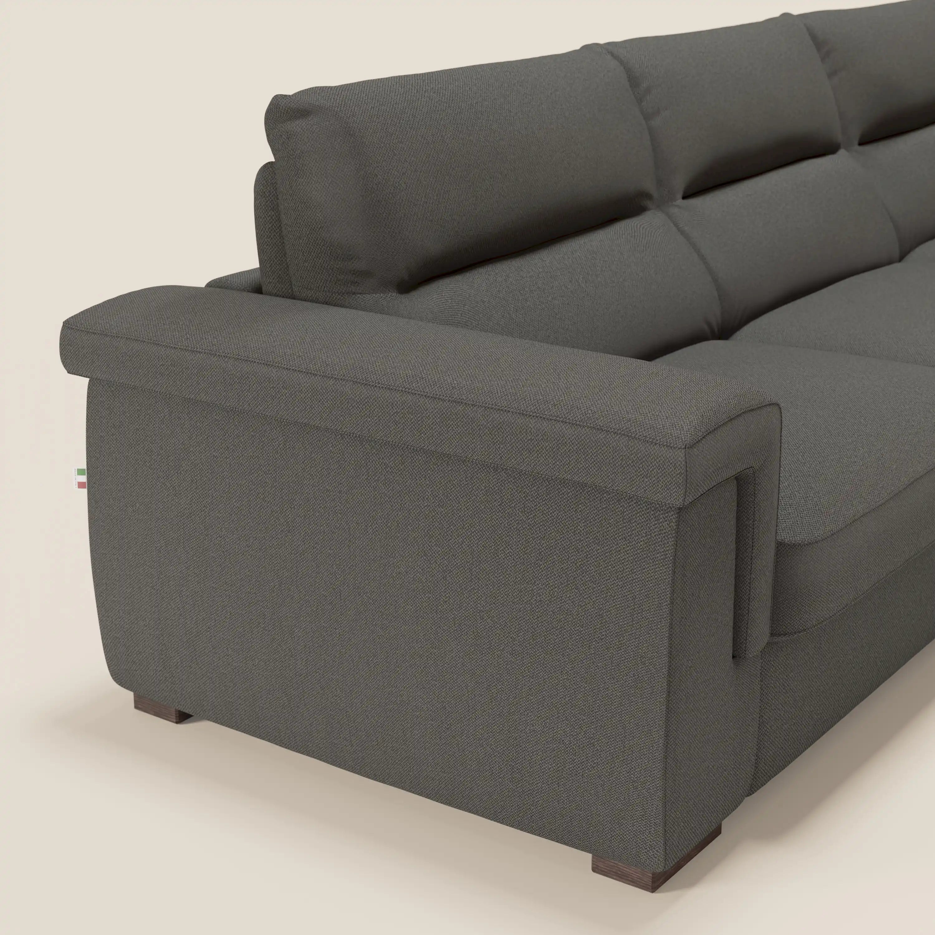 Primo piano del divano letto angolare Magnolia con Penisola Contenitore di Divani.Store in tessuto antracite antimacchia T05, con cuscini spessi, ampi braccioli, gambe corte in legno e sfondo beige chiaro.