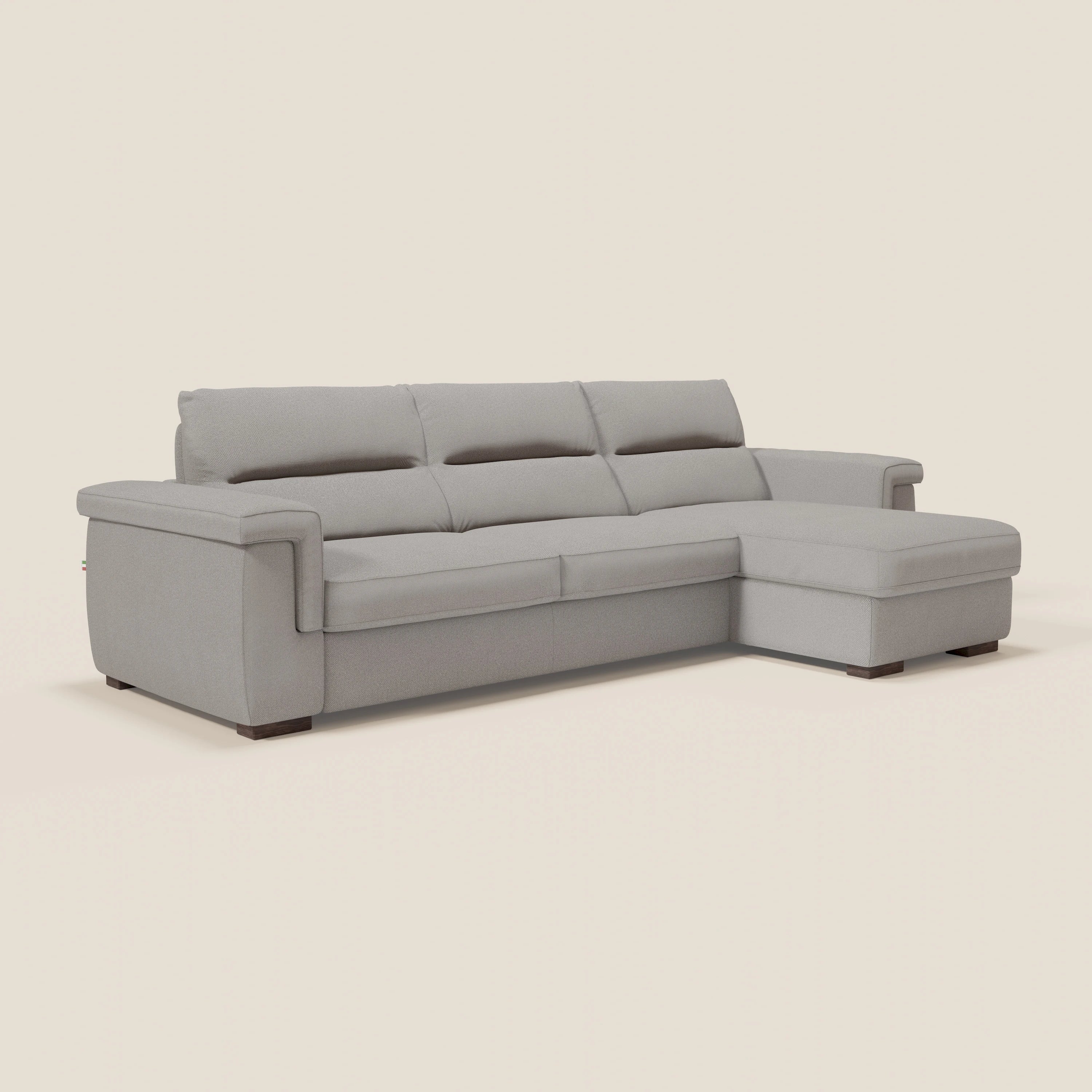 Il divano letto angolare Magnolia di Divani.Store è in tessuto smacchiabile grigio T05, con penisola contenitore a destra, ampi braccioli, tre cuscini schienale e materasso H18 cm. Gambe basse in legno scuro su sfondo crema neutro.