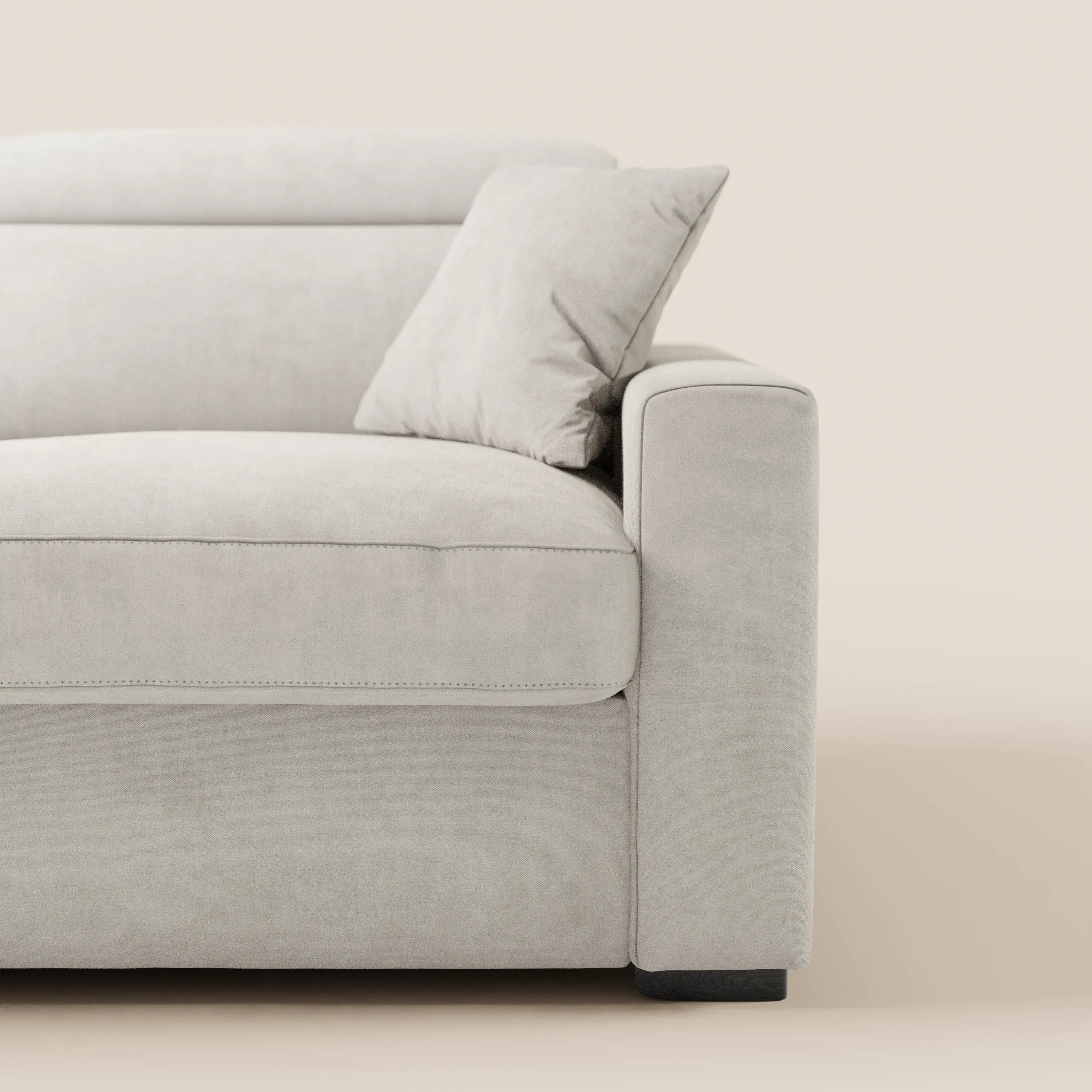 Un primo piano del divano letto a 3 posti Maximus di Divani.Store, realizzato in tessuto grigio chiaro Oeko-Tex antimacchia, con braccioli squadrati, cuscino coordinato, materasso alto 20 cm e poggiatesta regolabili, su uno sfondo beige.