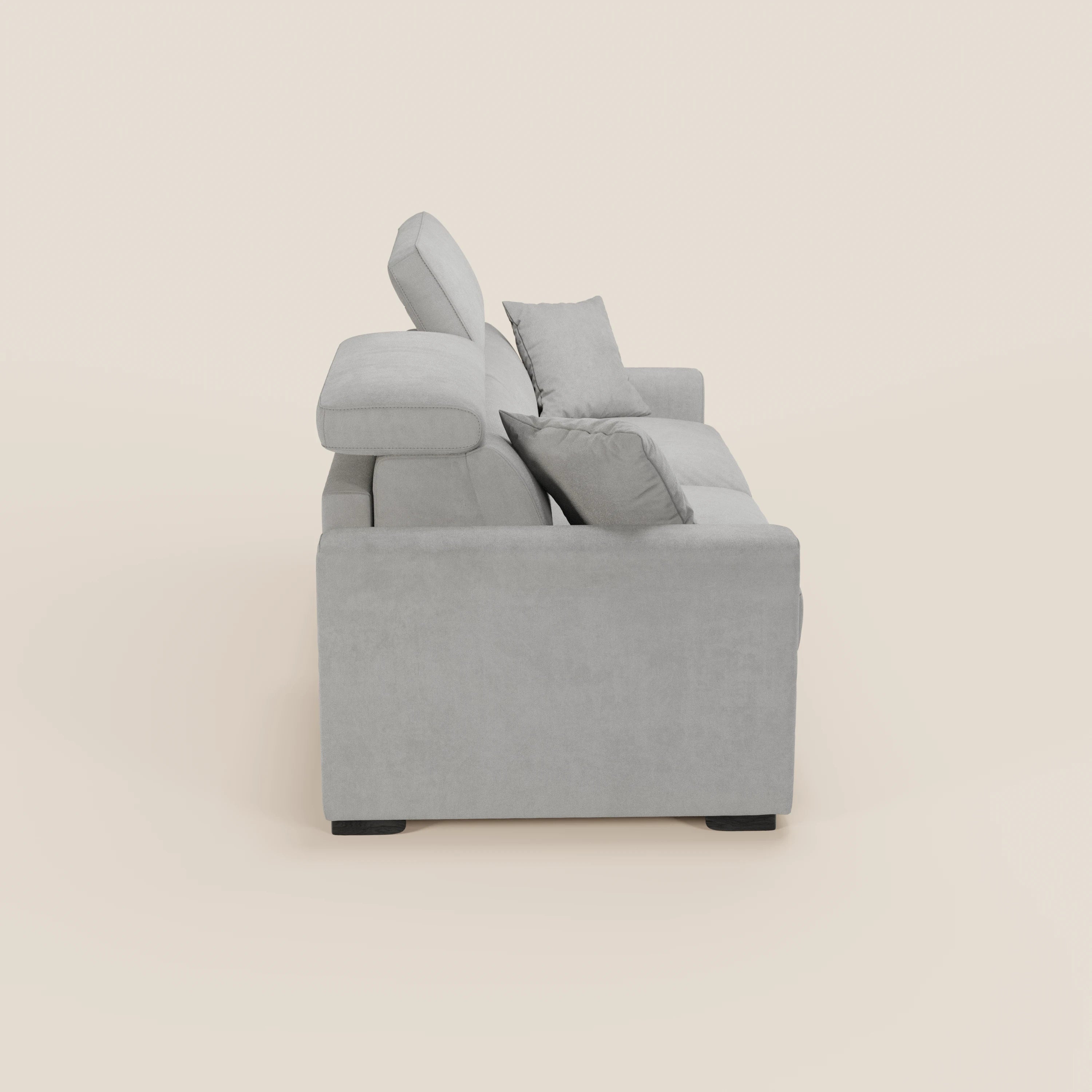 Vista laterale del divano letto a 3 posti Maximus con materasso ALTO 20 cm di Divani.Store, caratterizzato da poggiatesta reclinabili, braccioli squadrati, due cuscini di seduta e cuscini coordinati in tessuto Oeko-Tex grigio chiaro su uno sfondo crema chiaro.