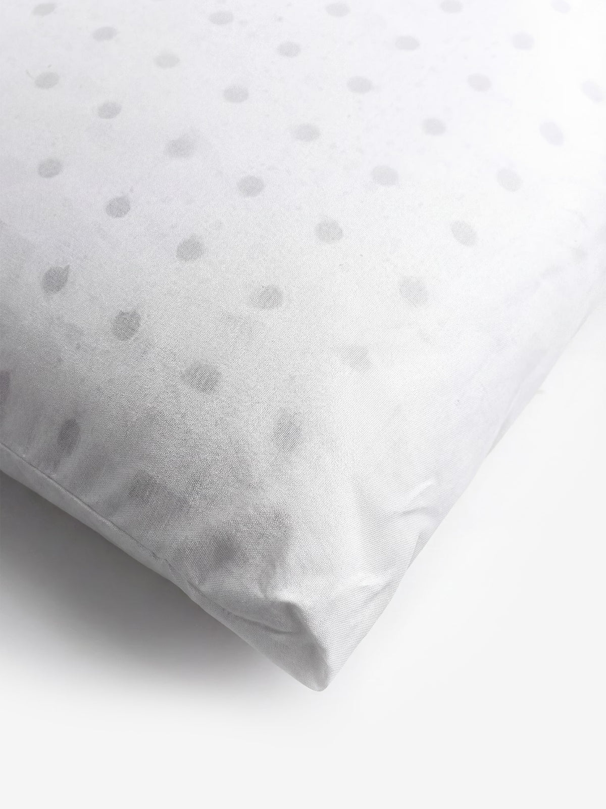 Un primo piano del cuscino KYROS-PRIME in memory foam iniettato, personalizzato e ortopedico di Divani.Store mette in risalto la sua fodera bianca con un delicato motivo a pois. I puntini grigio chiaro sono distribuiti in modo uniforme sul tessuto liscio, conferendogli un aspetto delicato e strutturato. Progettato per il supporto cervicale, l’angolo di questo cuscino ortopedico risalta sullo sfondo bianco a tinta unita.