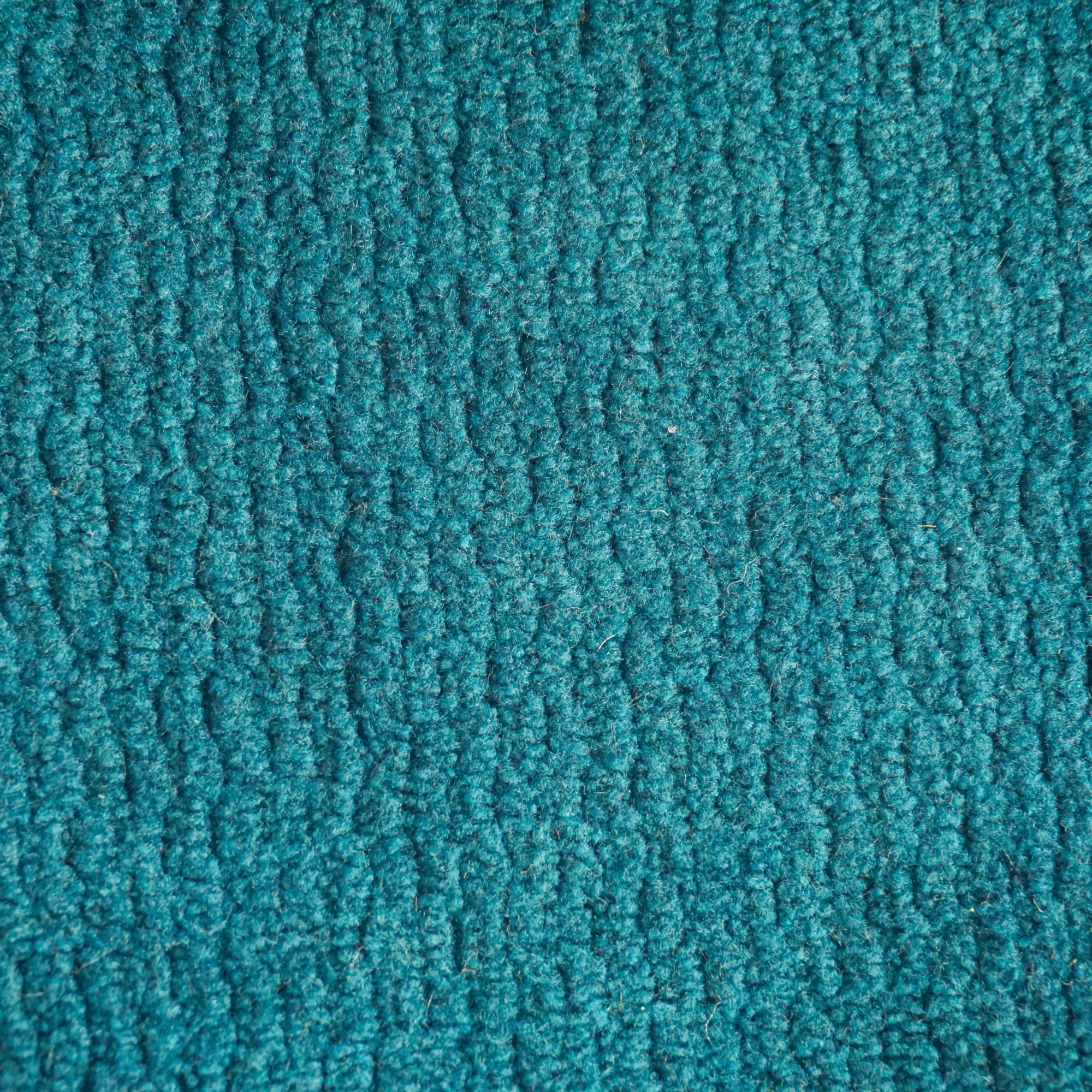 Primo piano di Personalizzazione in T32 di Divani.Store: un tappeto blu acqua caratterizzato da una superficie strutturata e anellata con motivi in rilievo e ripetuti. Le fibre a trama fitta e l'illuminazione ne enfatizzano il colore vibrante e la ricchezza di dettagli.