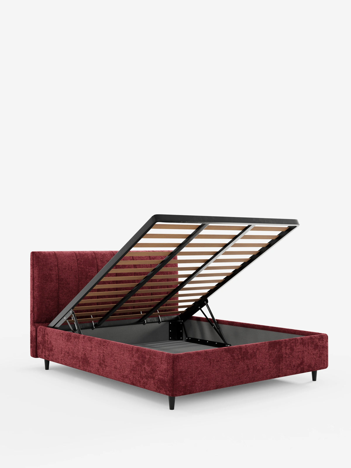 Un letto imbottito ONYX con contenitore e testiera verticale in tessuto certificato Oeko-Tex® color rosso scuro, caratterizzato da un’alta testiera a pannelli verticali, raffigurato in un monolocale con la rete a doghe sollevata e appoggiata su quattro piccoli piedini neri.
