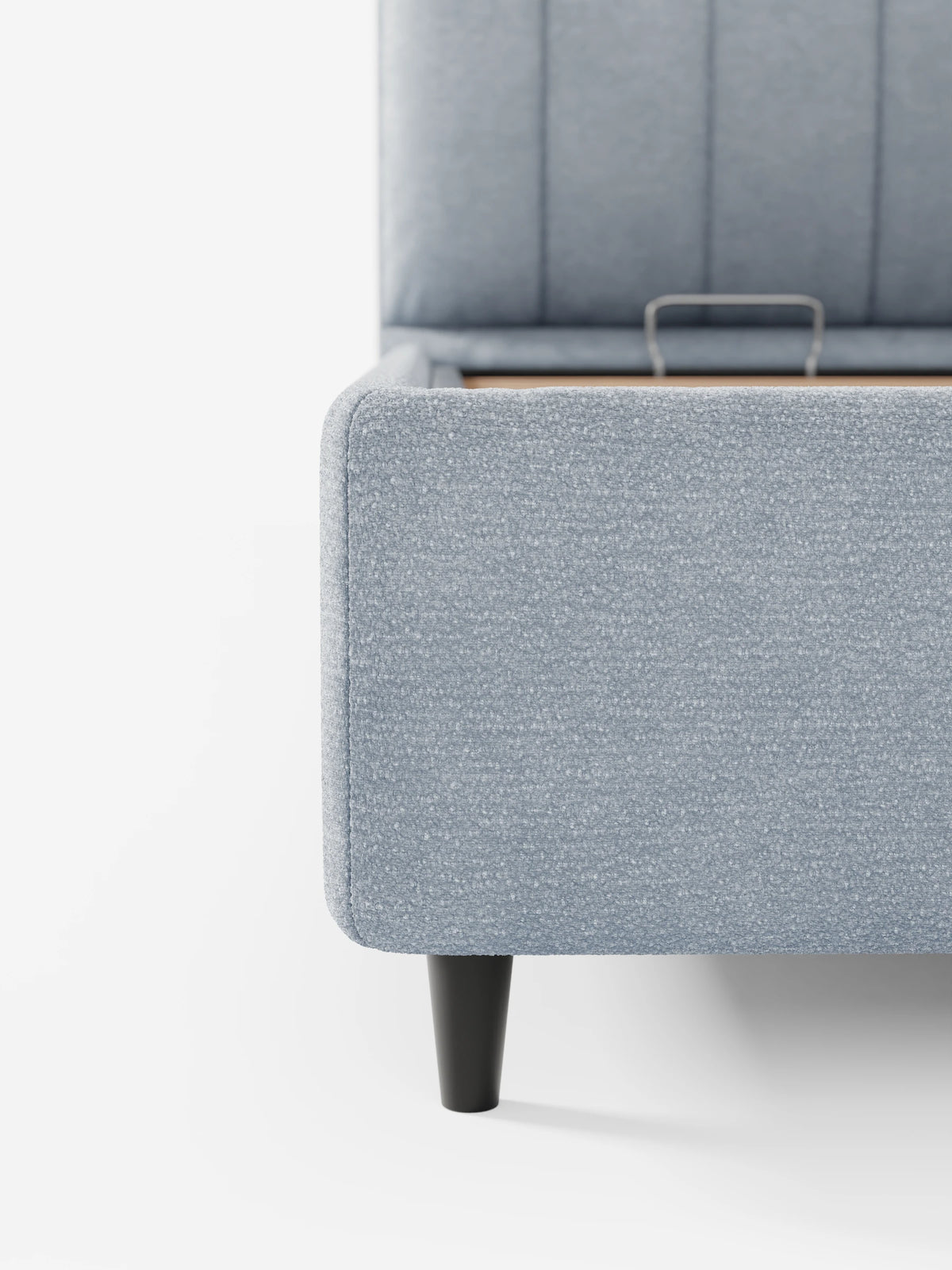 Il letto imbottito ONYX con contenitore e testiera verticale in tessuto certificato Oeko-Tex® è un letto contenitore di colore azzurro con testiera dalle cuciture verticali su gambe affusolate, raffigurato con la base del materasso sollevata per mostrare il vano contenitore.