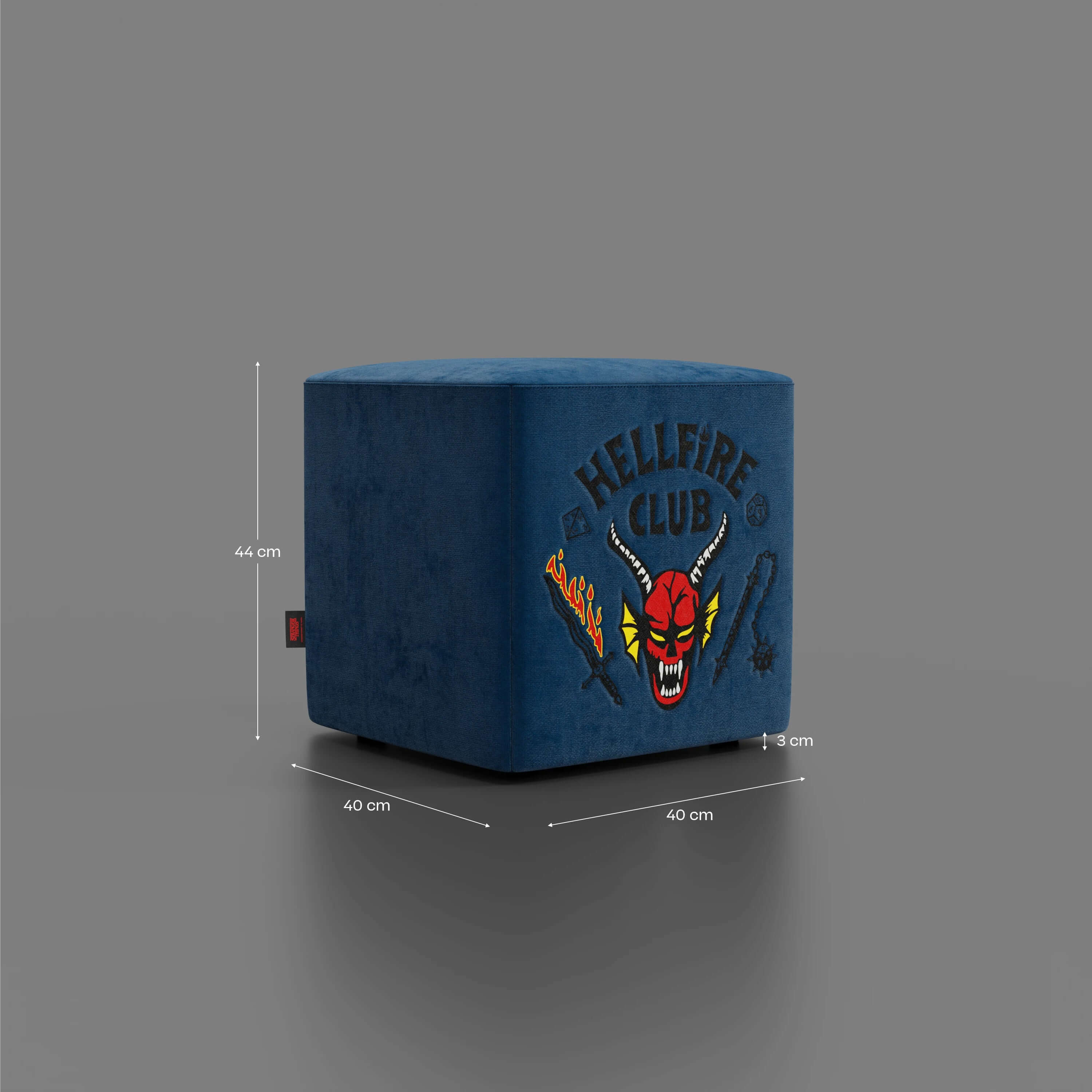 Il pouf Cube Hellfire club Stranger Things Edition di Divani.Store è un pouf quadrato in velluto blu (44x40 cm) con il logo "HELLFIRE CLUB" in grassetto e un'opera d'arte vivace, un pezzo di design iconico e in edizione limitata su sfondo grigio.