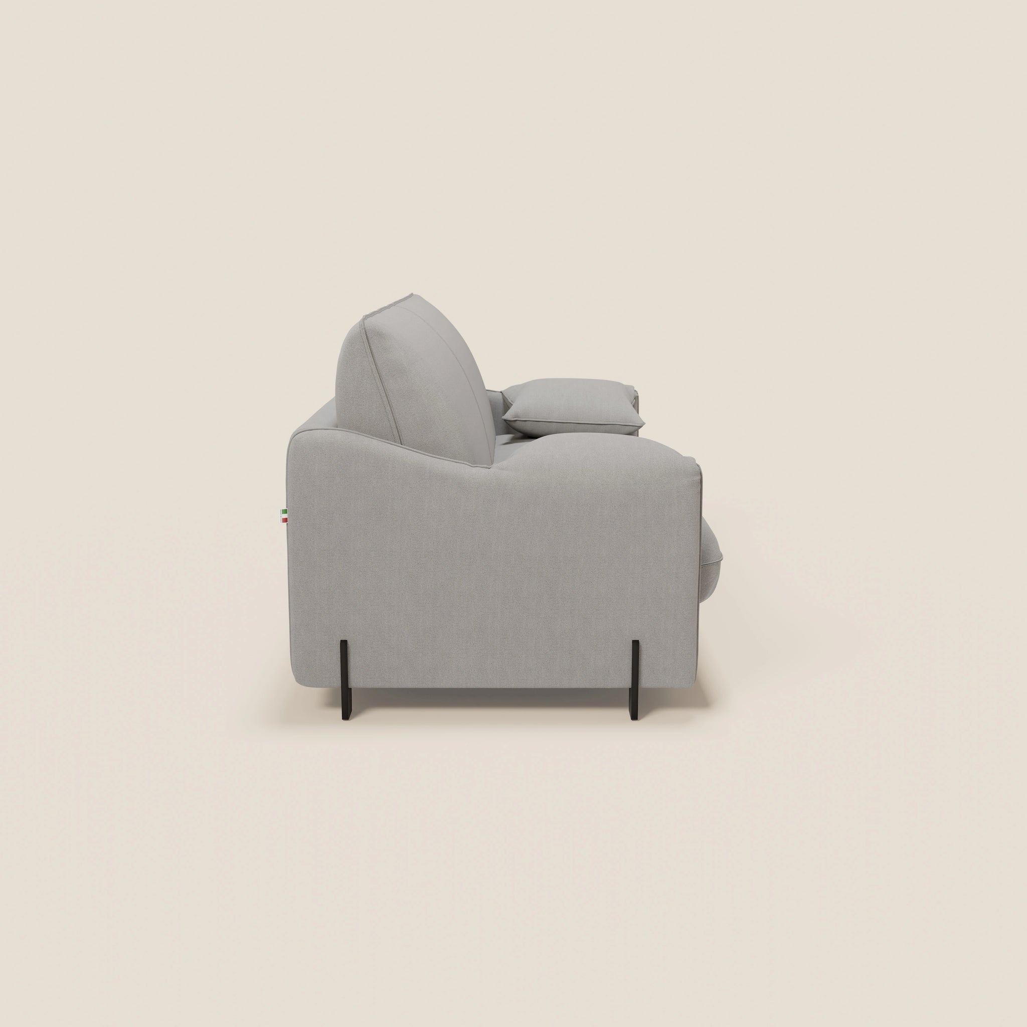 Vista laterale minimalista del divano letto Primula da 177 cm di Divani.Store in tessuto smacchiabile T05 GRIGIO, con cuscini spessi, braccioli mobili, materasso alto 18 cm, sottili gambe in metallo nero, il tutto su uno sfondo semplice bianco sporco.