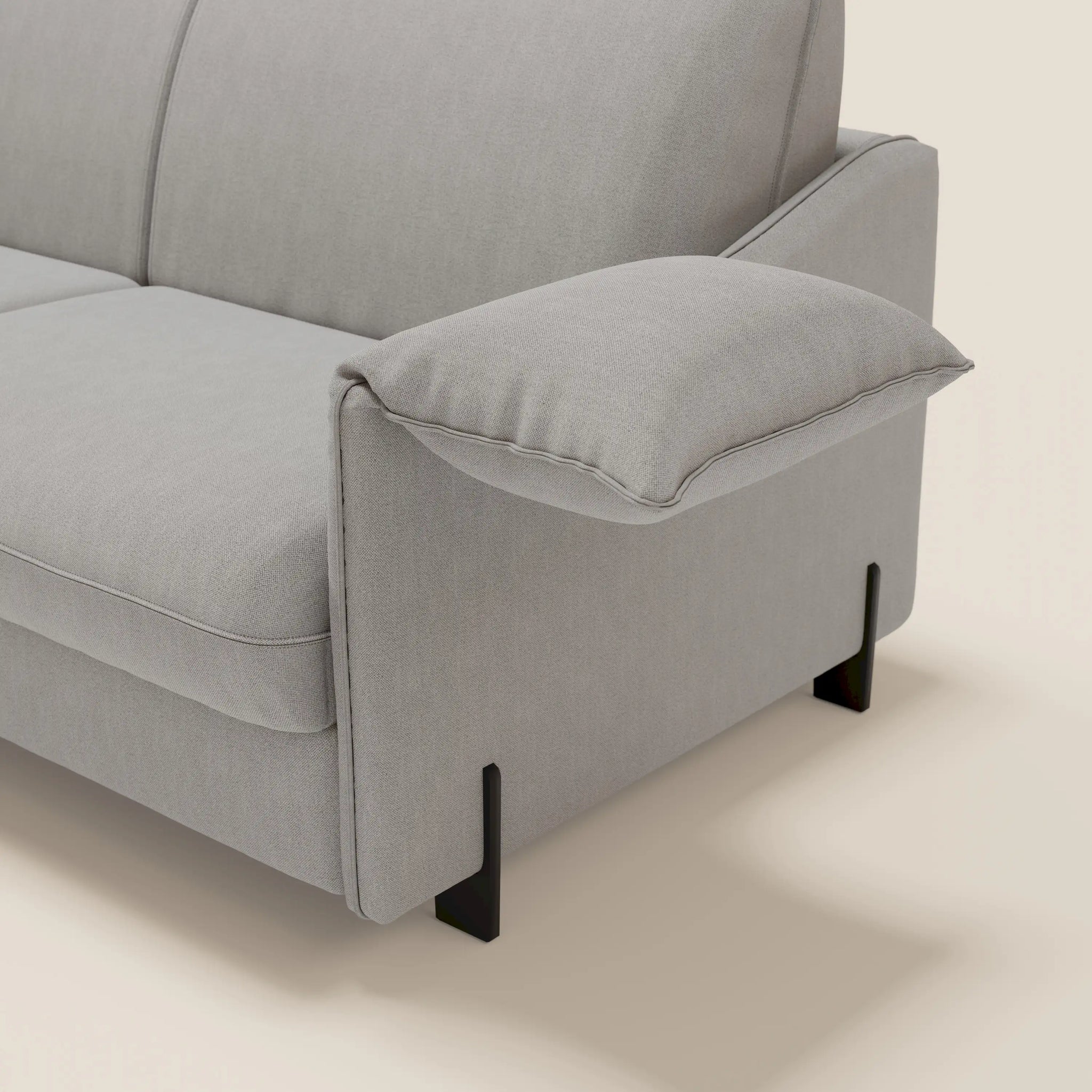 Un primo piano del divano letto Primula da 177 cm di Divani.Store in tessuto lavabile grigio T05 mette in risalto i morbidi braccioli mobili e le gambe in metallo nero, fondendo stile moderno e comfort contemporaneo su uno sfondo beige chiaro.