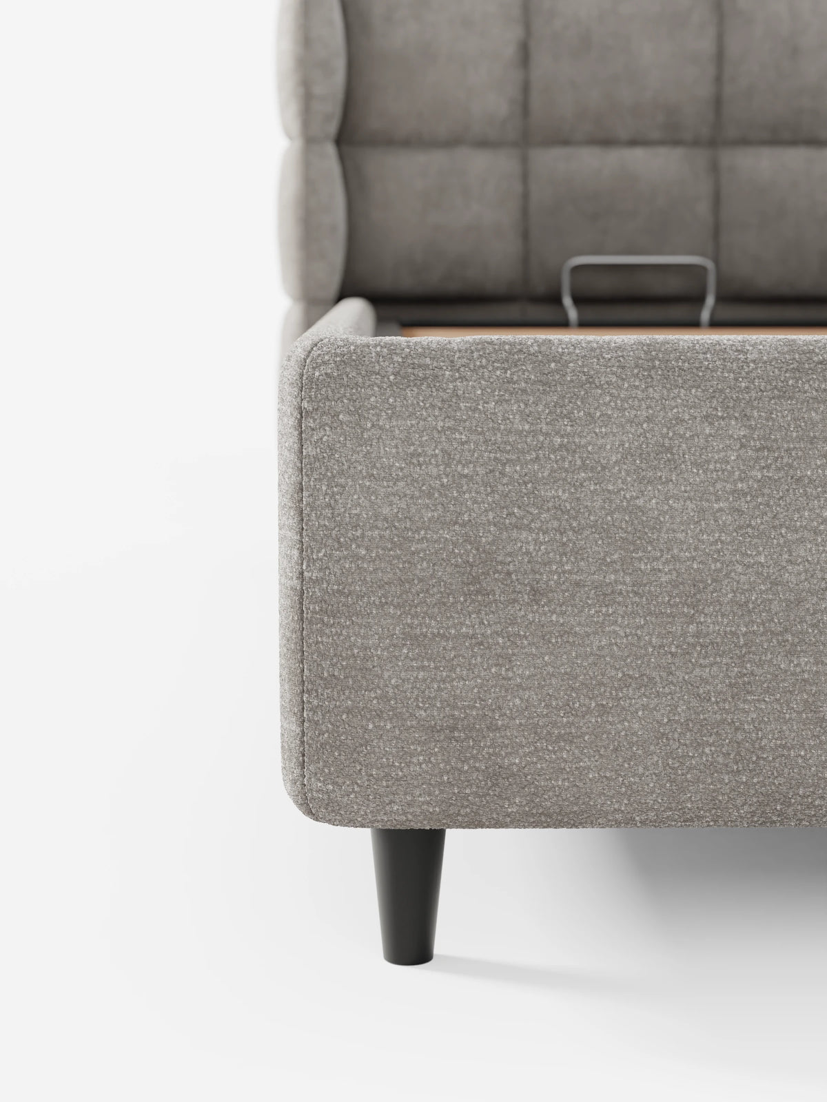 Un primo piano di un letto imbottito RAGNAR color taupe con vano contenitore e testiera capitonné avvolgente, dotato di base rialzata, che rivela un vano contenitore in legno su gambe corte e affusolate di colore nero, su uno sfondo bianco a tinta unita.