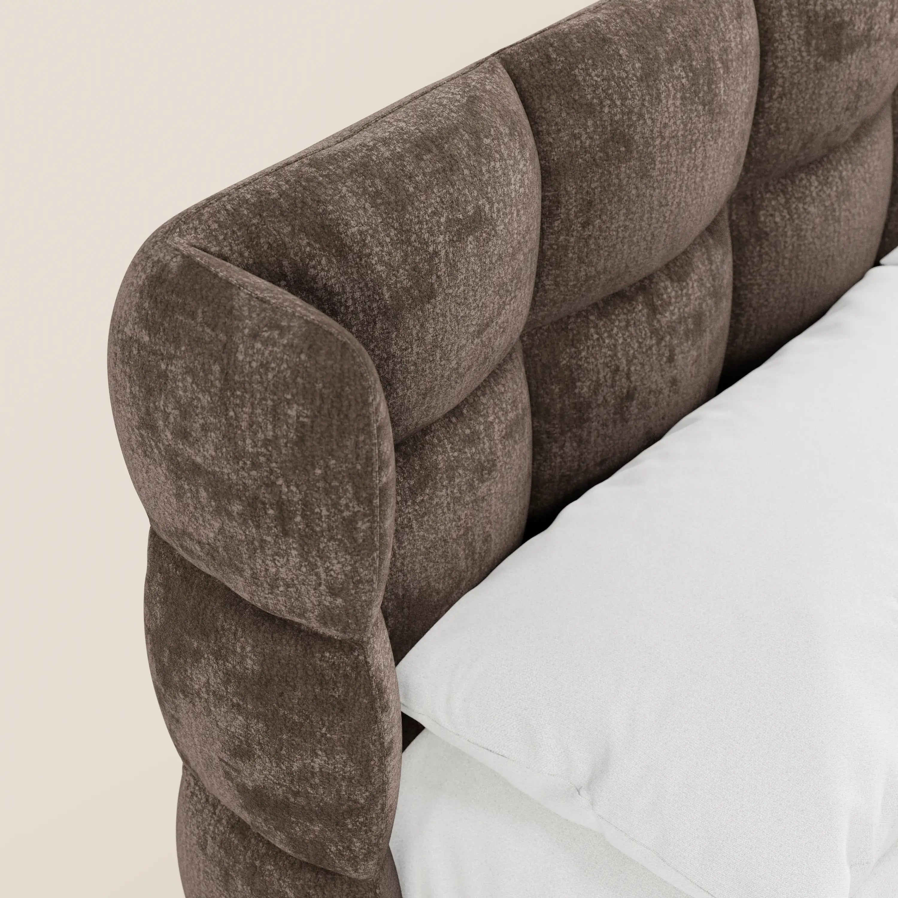 Un primo piano del letto imbottito RAGNAR con contenitore e testiera capitonné avvolgente di Letti.store, realizzato in elegante tessuto certificato Oeko-Tex®, mostra la testiera con segmenti arrotondati e imbottiti, abbinata al materasso e alla biancheria da letto bianca.