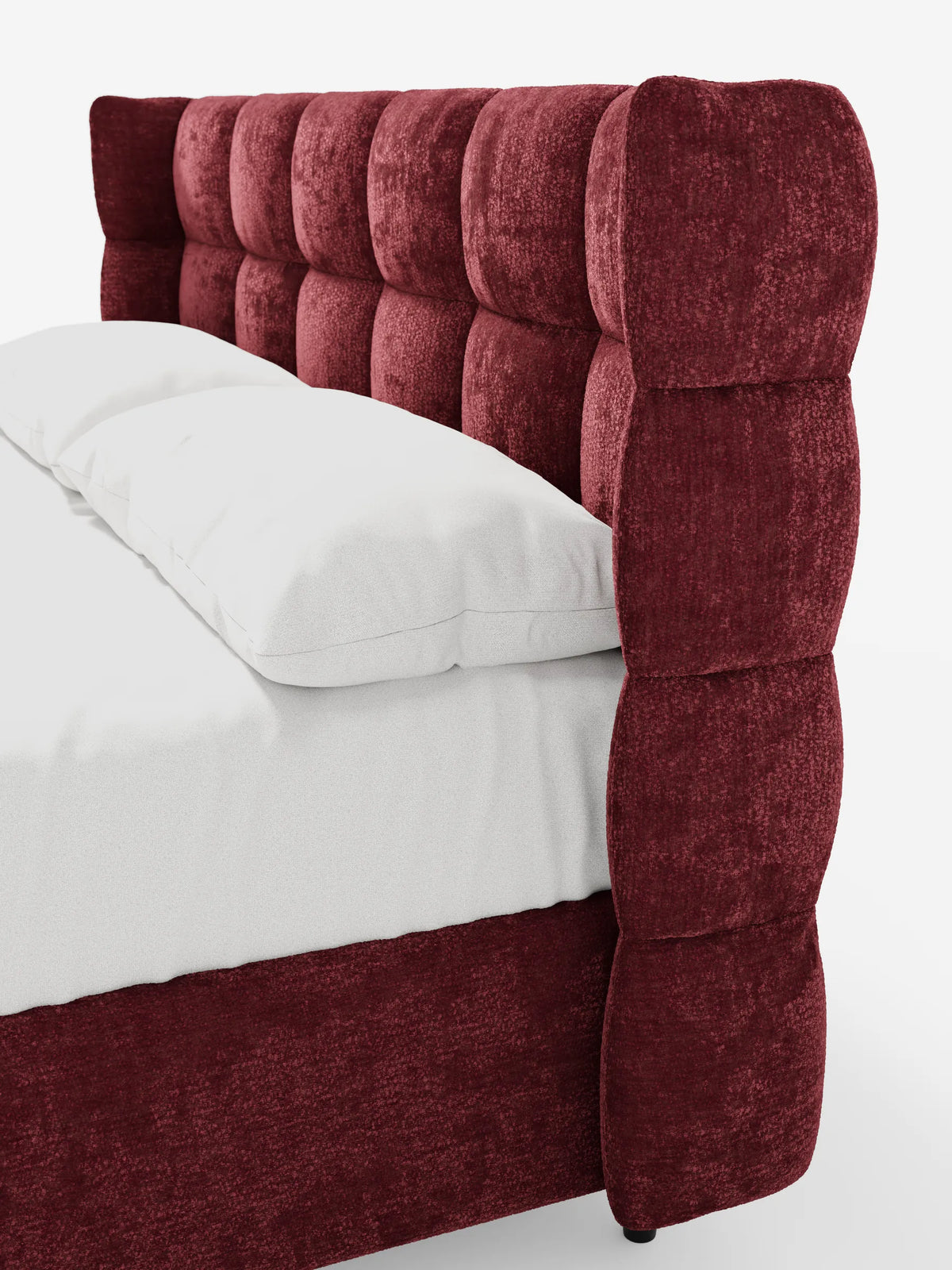 Un letto RAGNAR di colore rosso intenso, con rivestimento a ciuffetti, imbottito, dotato di vano contenitore e testiera capitonné avvolgente, rivestito con lenzuola bianche immacolate e due cuscini su uno sfondo bianco a tinta unita.
