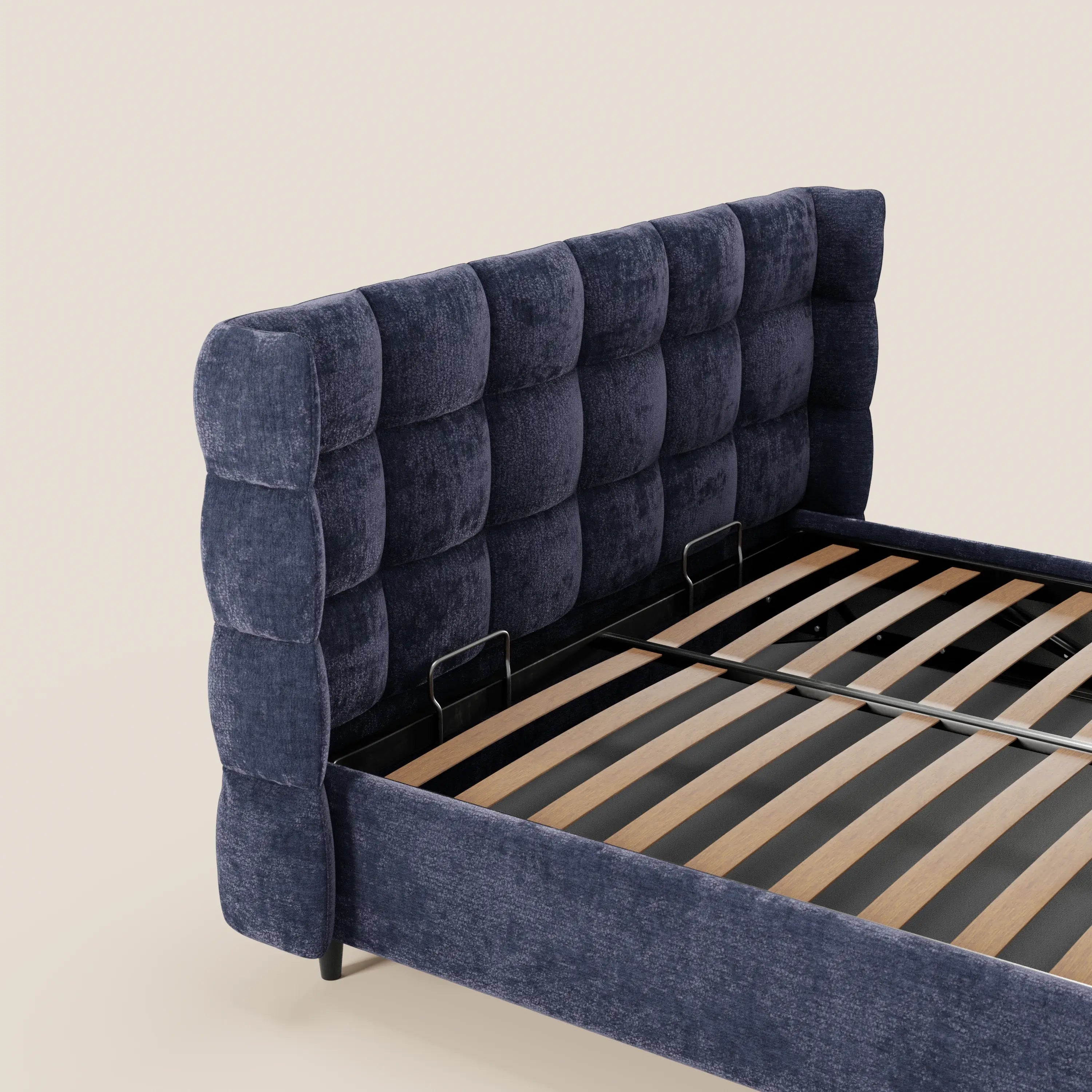 Il letto imbottito RAGNAR di Letti.store presenta una testiera alta e avvolgente, di colore blu intenso, con rivestimento capitonné in tessuto Oeko-Tex®, eleganti doghe in legno a vista e uno sfondo semplice color beige chiaro.