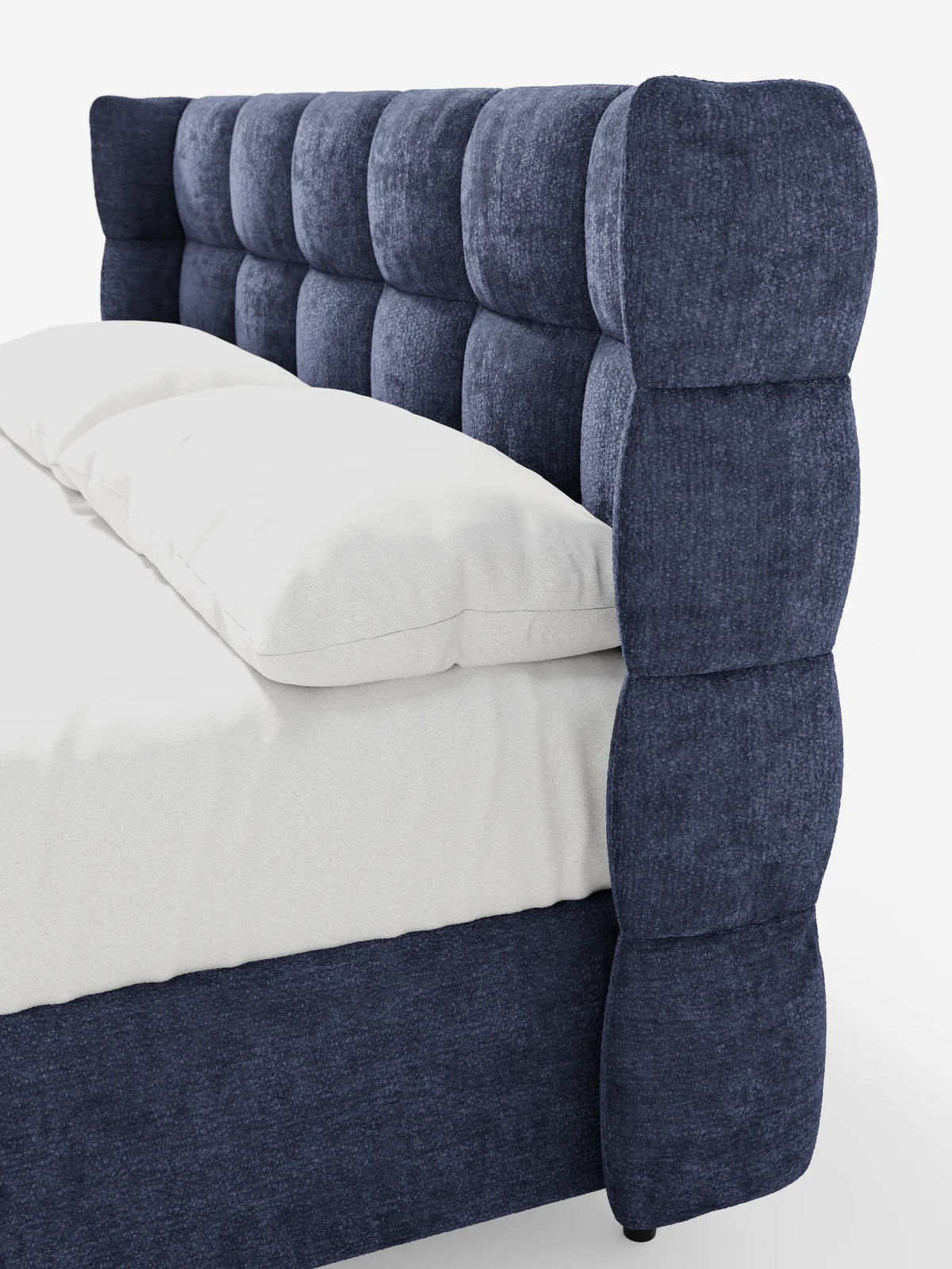 Un letto imbottito RAGNAR blu scuro con contenitore e testiera capitonné avvolgente, caratterizzata da un'alta testiera trapuntata, tessuto testurizzato, biancheria da letto candida e un motivo a griglia profonda sulla struttura imbottita, vista di profilo.