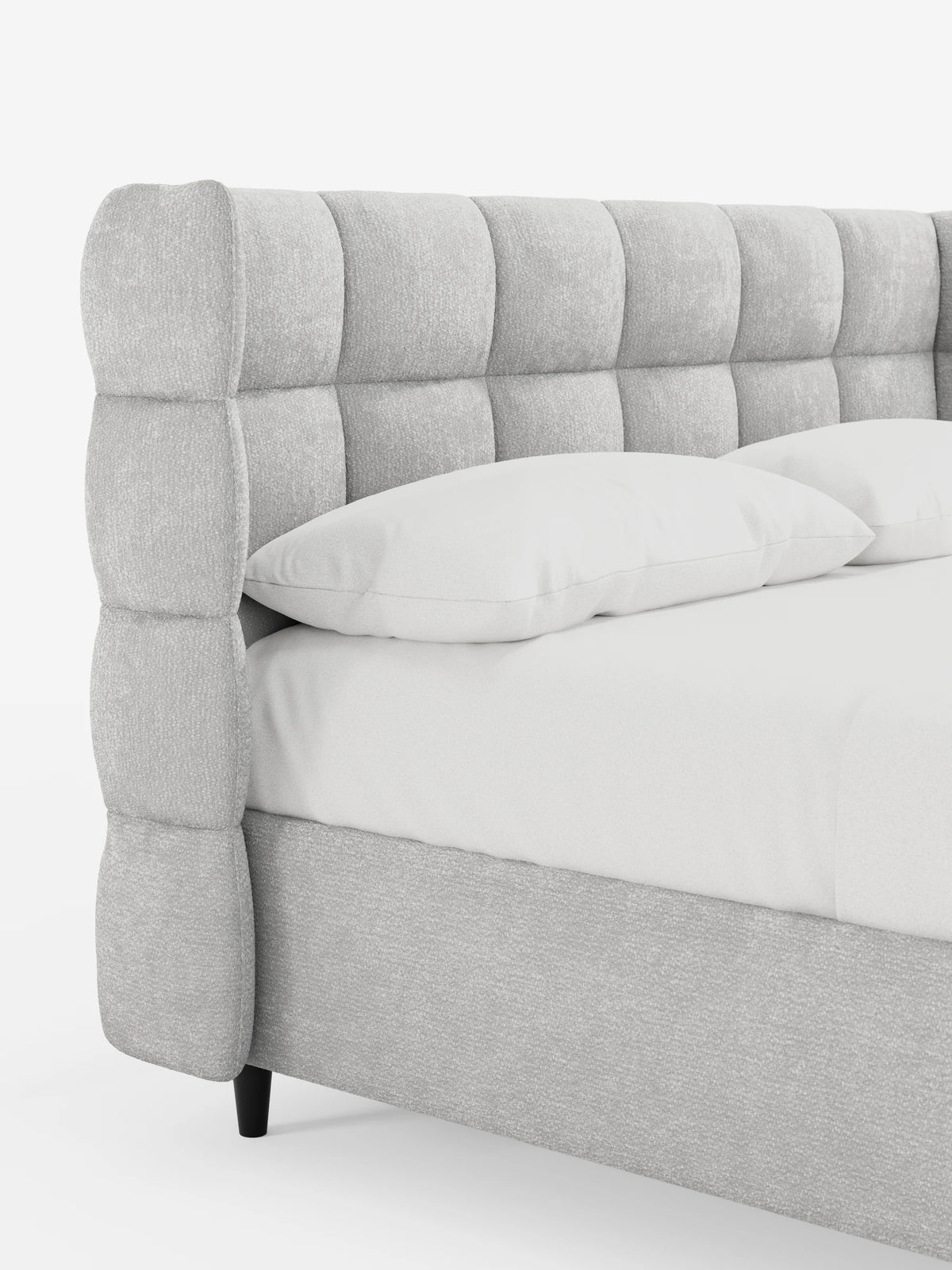 Un primo piano di un letto RAGNAR grigio chiaro, imbottito, con contenitore e testiera capitonné avvolgente, caratterizzata da un design a quadratini trapuntati, su uno sfondo chiaro con due cuscini bianchi.