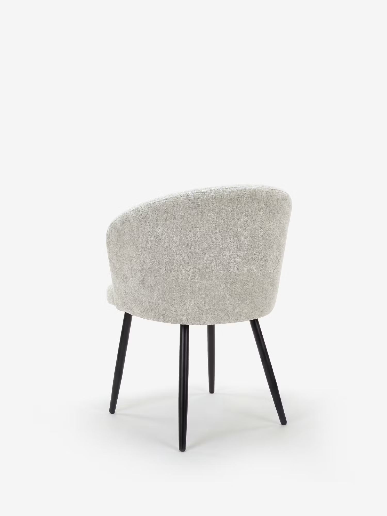 La sedia Rovo con braccioli di Divani.Store presenta uno schienale e una seduta curvi rivestiti in ciniglia grigio chiaro, con sottili gambe in metallo nero. Ripresa da dietro con una leggera angolazione, il suo design moderno risalta sullo sfondo bianco.