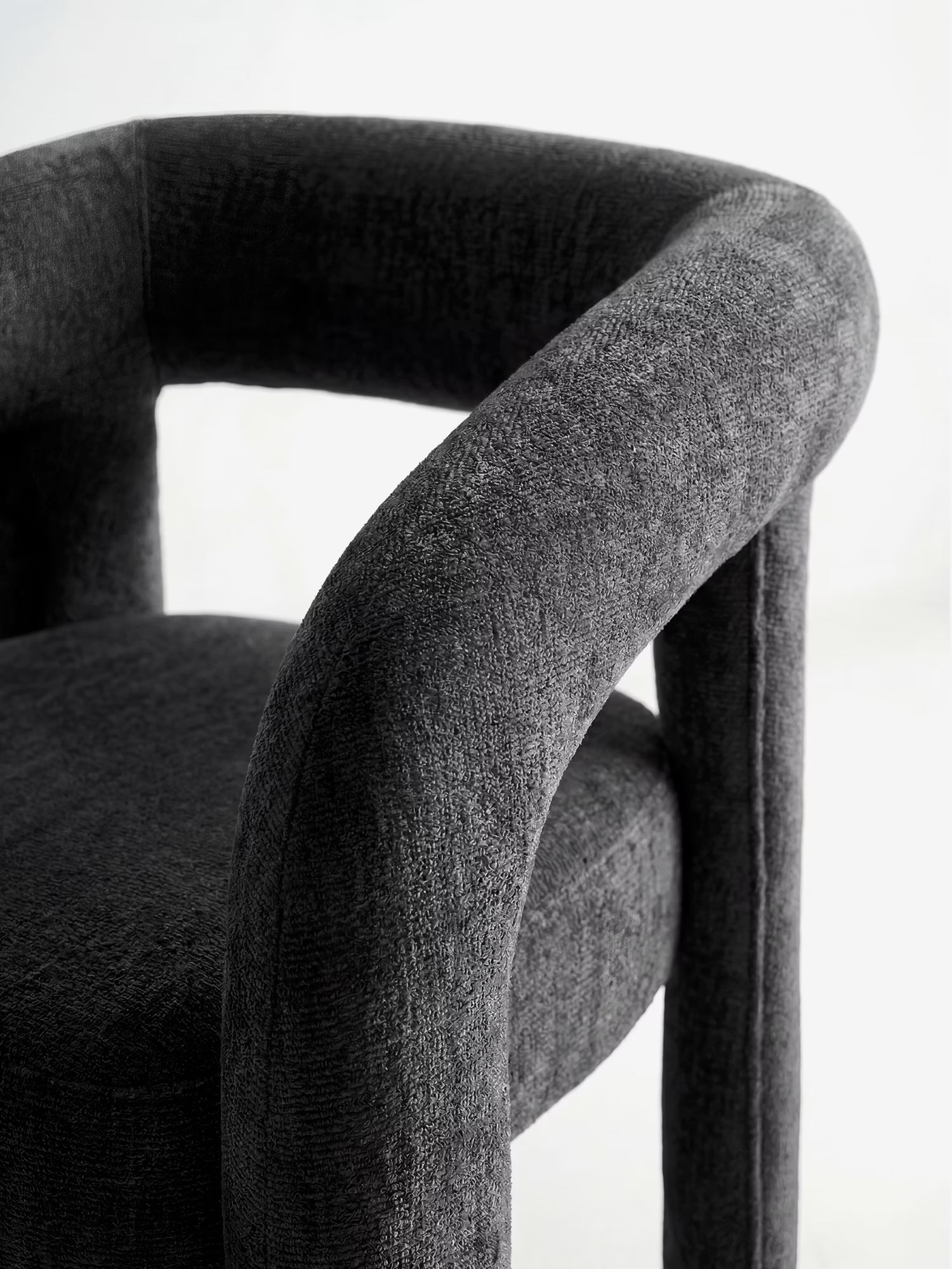 Primo piano della sedia di design imbottita “Sibilla” di Divani.Store, con struttura rivestita, schienale e braccioli ad arco in tessuto grigio scuro testurizzato. Design contemporaneo dalle linee morbide su sfondo bianco.