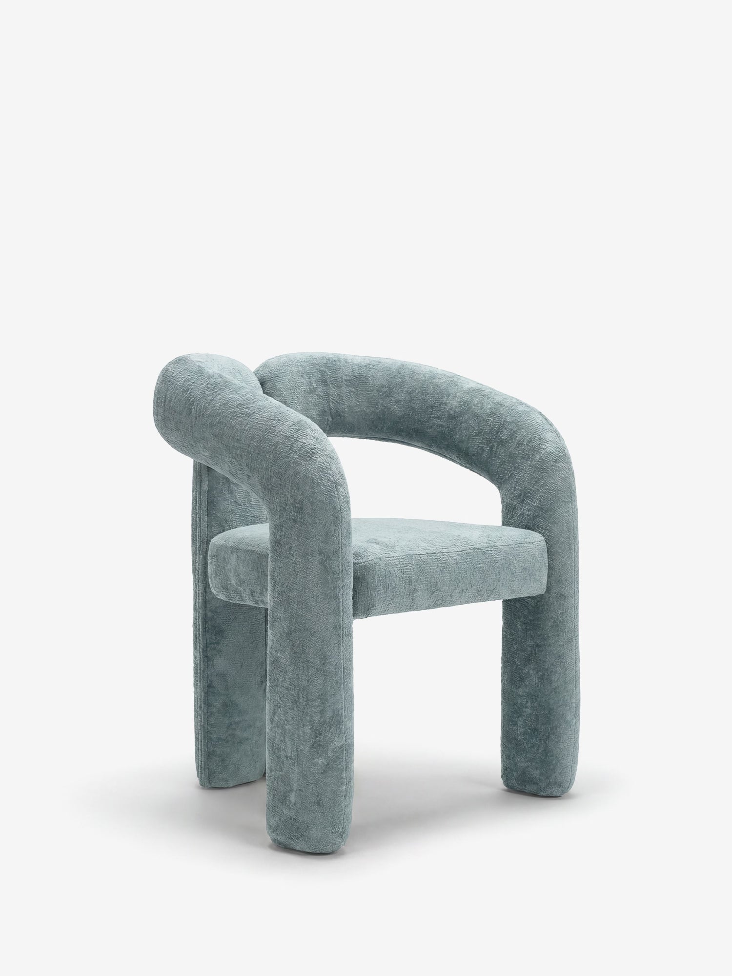 La sedia di design Sibilla di Divani.Store presenta una struttura arcuata interamente imbottita, gambe tubolari di grosso spessore, braccioli e schienale rivestiti in morbido tessuto dalla trama ruvida nei toni del grigio-azzurro, il tutto su uno sfondo chiaro e sobrio.