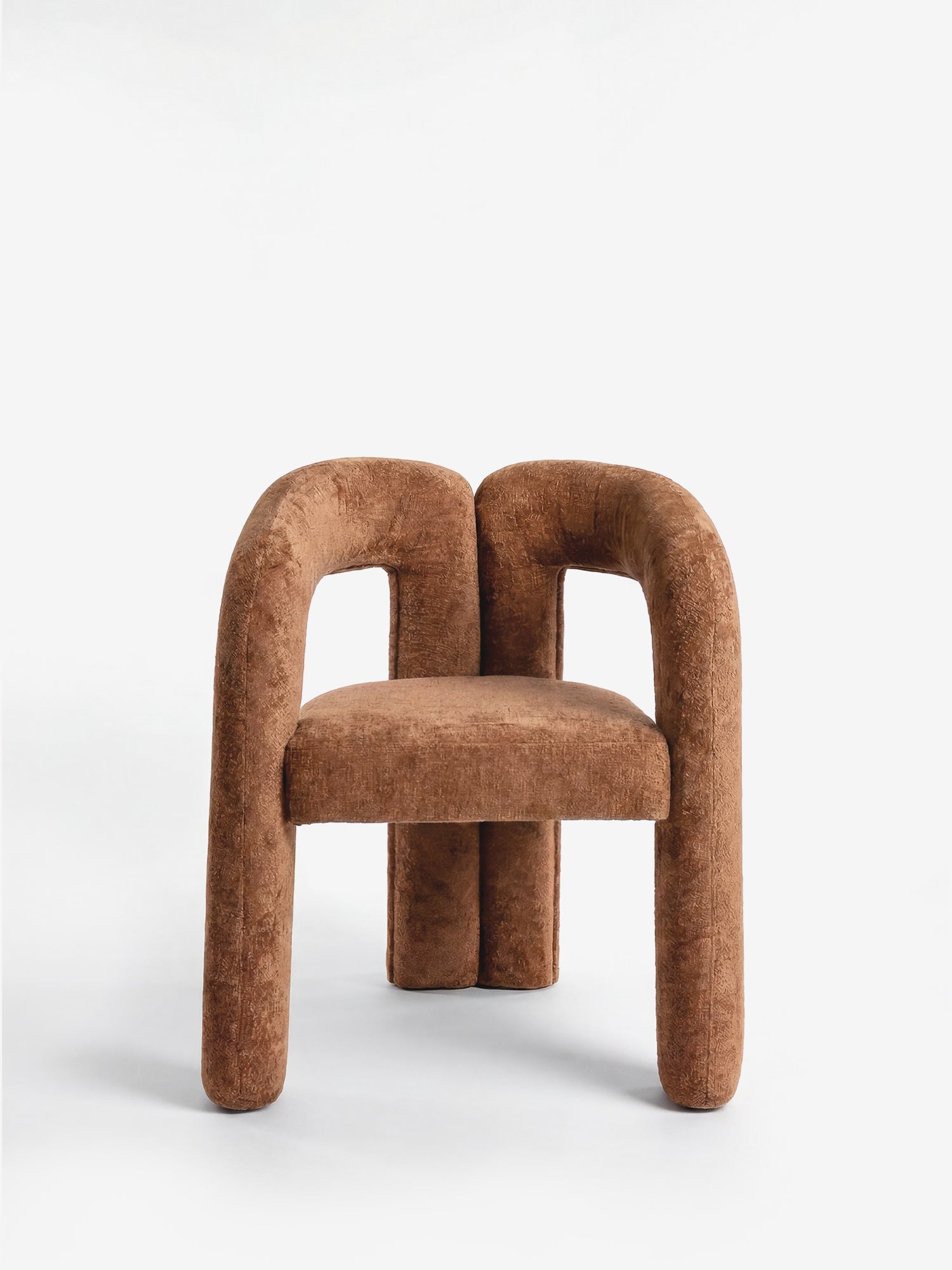 La sedia di design imbottita Sibilla di Divani.Store presenta una forma ad arco moderna, con struttura interamente rivestita in tessuto marrone e linee geometriche scultoree, perfetta come elemento d'arredo contemporaneo.